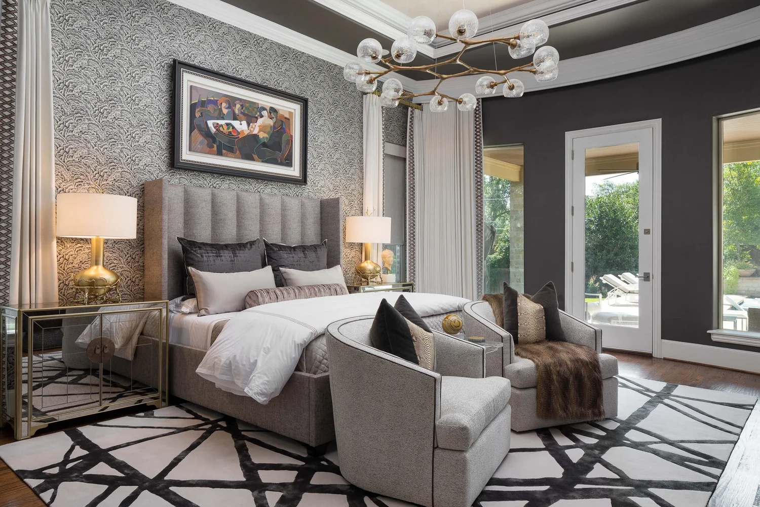Primary bedroom with a channel-tufted headboard, branch chandelier and swivel chairs, designed by Ricky Phillips of Homeology