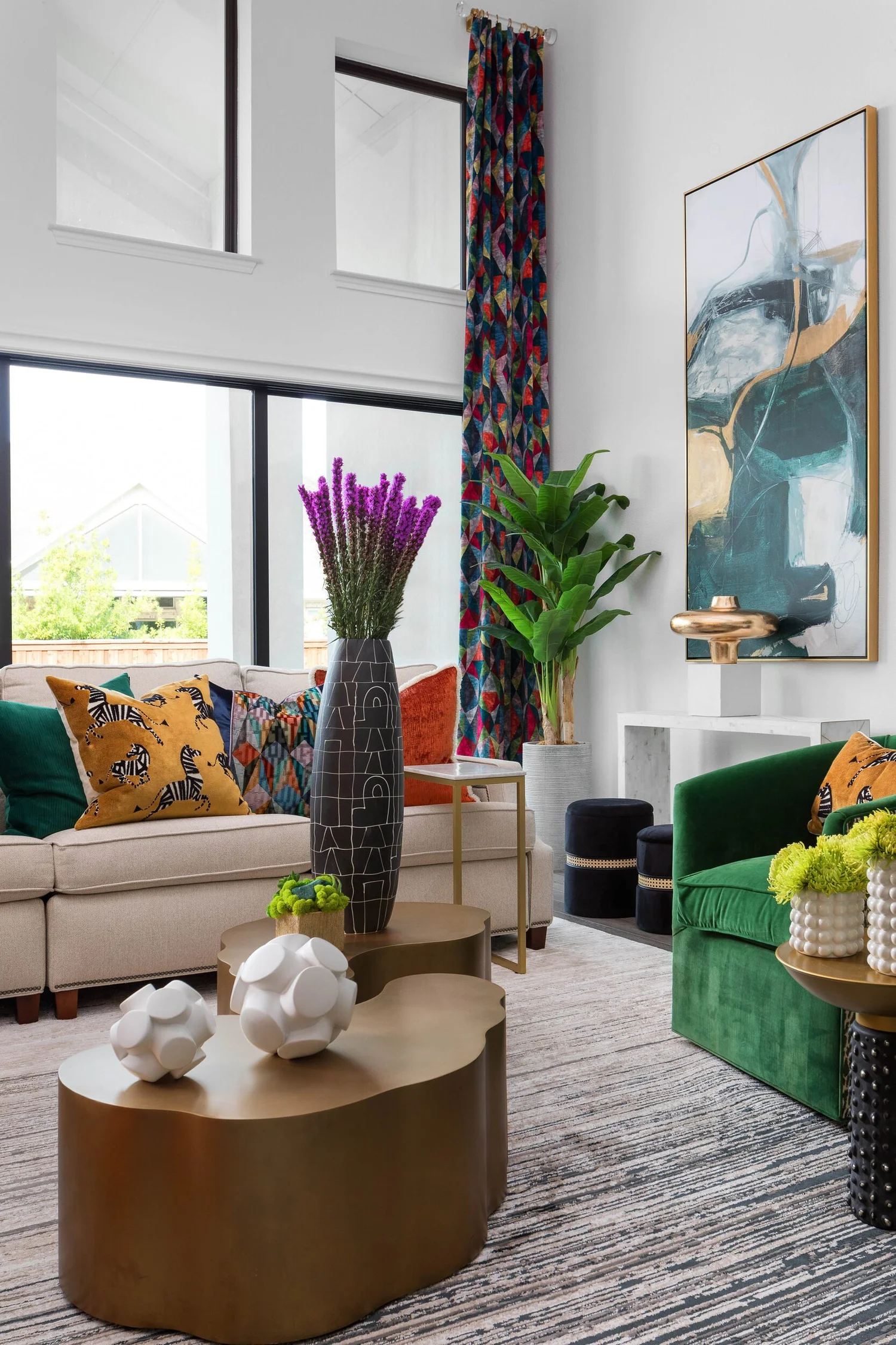 Living room seen from the side, with tall windows, patterned drapery and a bronze coffee table