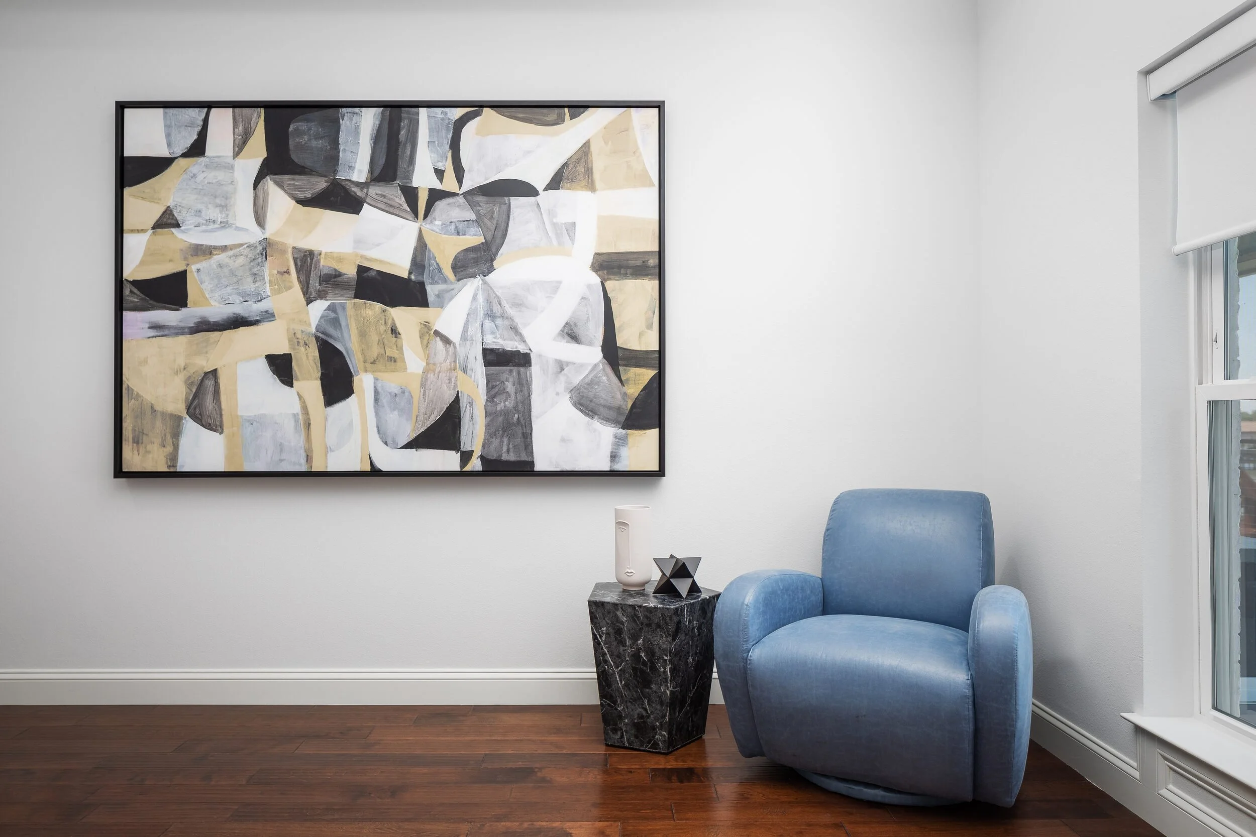 Blue leather swivel chair beneath a large black, gold and gray abstract painting