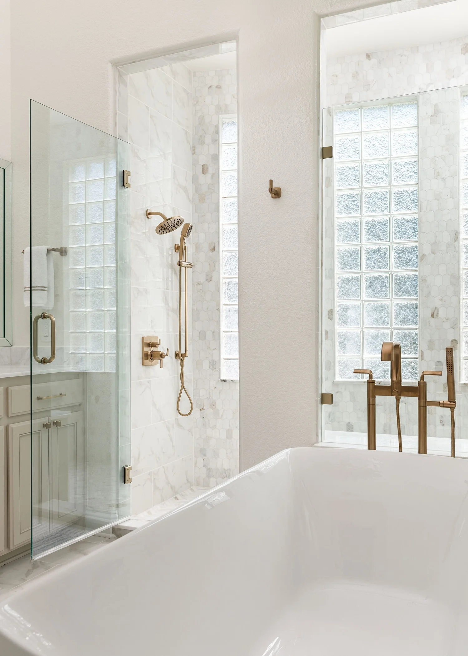 Glass shower enclosure beside the freestanding tub and brass floor-mount faucet