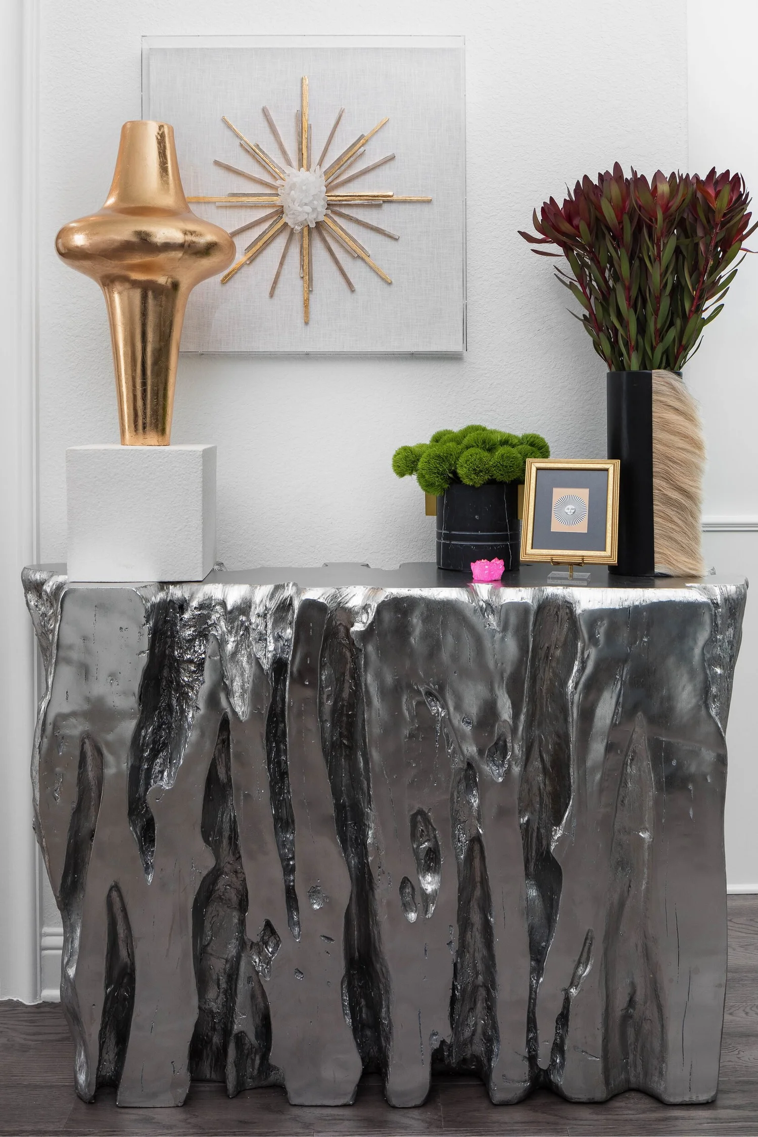 Silver sculptural console with a gold starburst mirror and copper vase