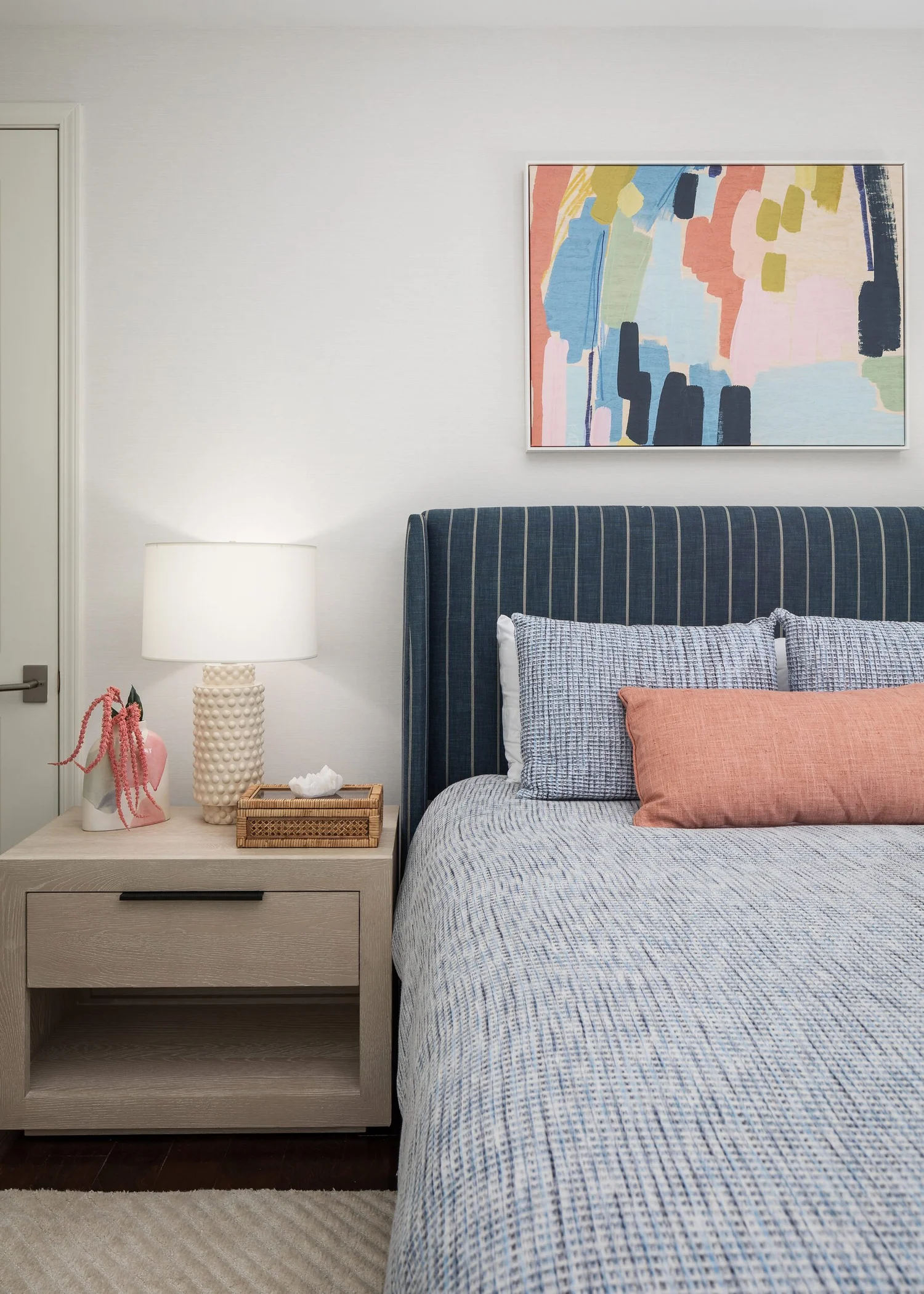 Navy striped headboard and nightstand lamp below pastel abstract art
