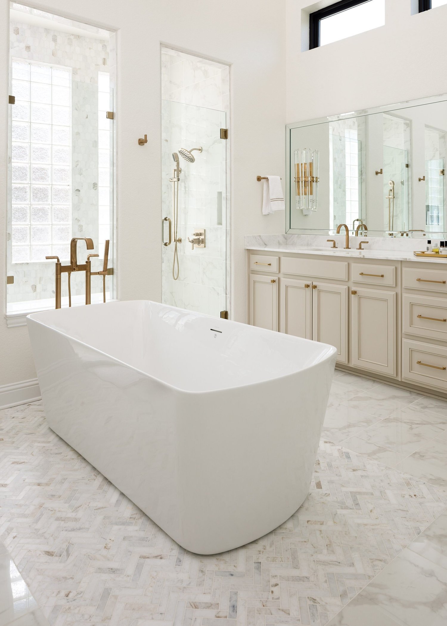 Freestanding tub on herringbone marble with the vanity beyond