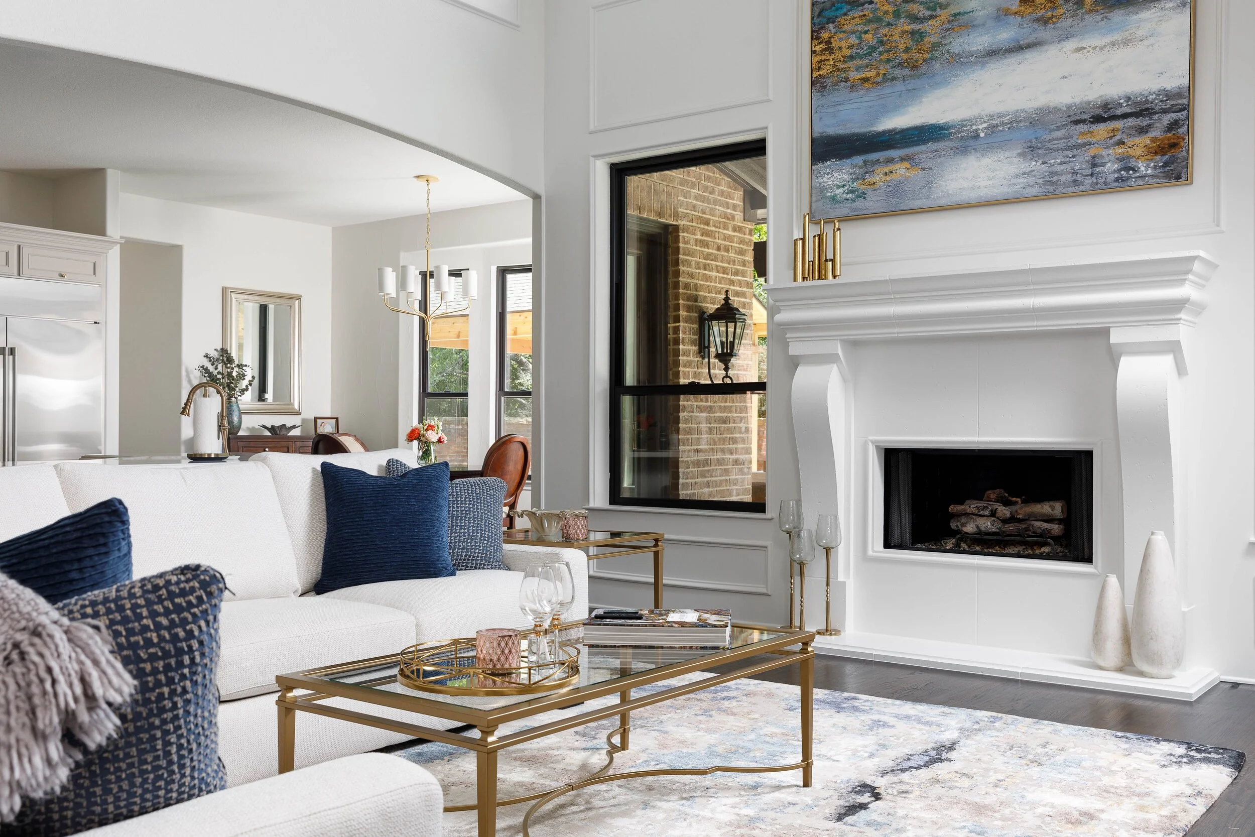 Living room with a white sectional, brass coffee table and abstract art above the fireplace