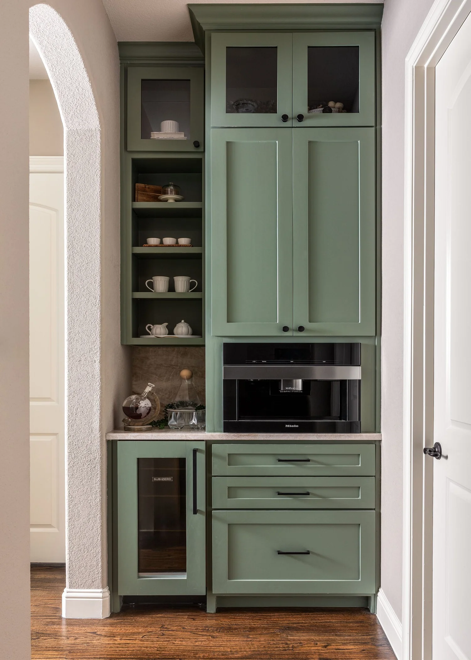 Built-in coffee bar in sage green cabinetry with glass upper doors