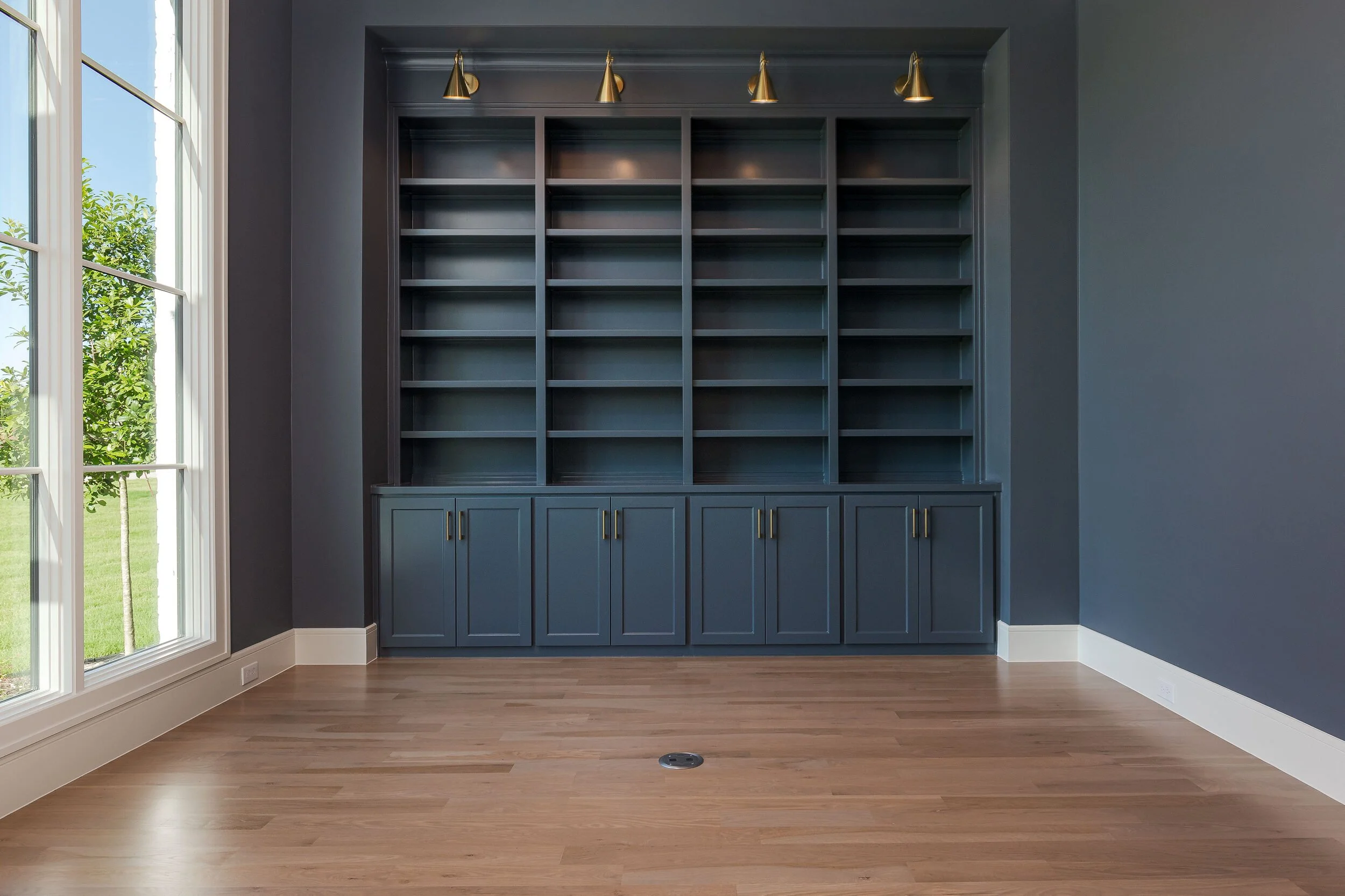 Study with floor-to-ceiling navy built-ins, brass picture lights and tall windows
