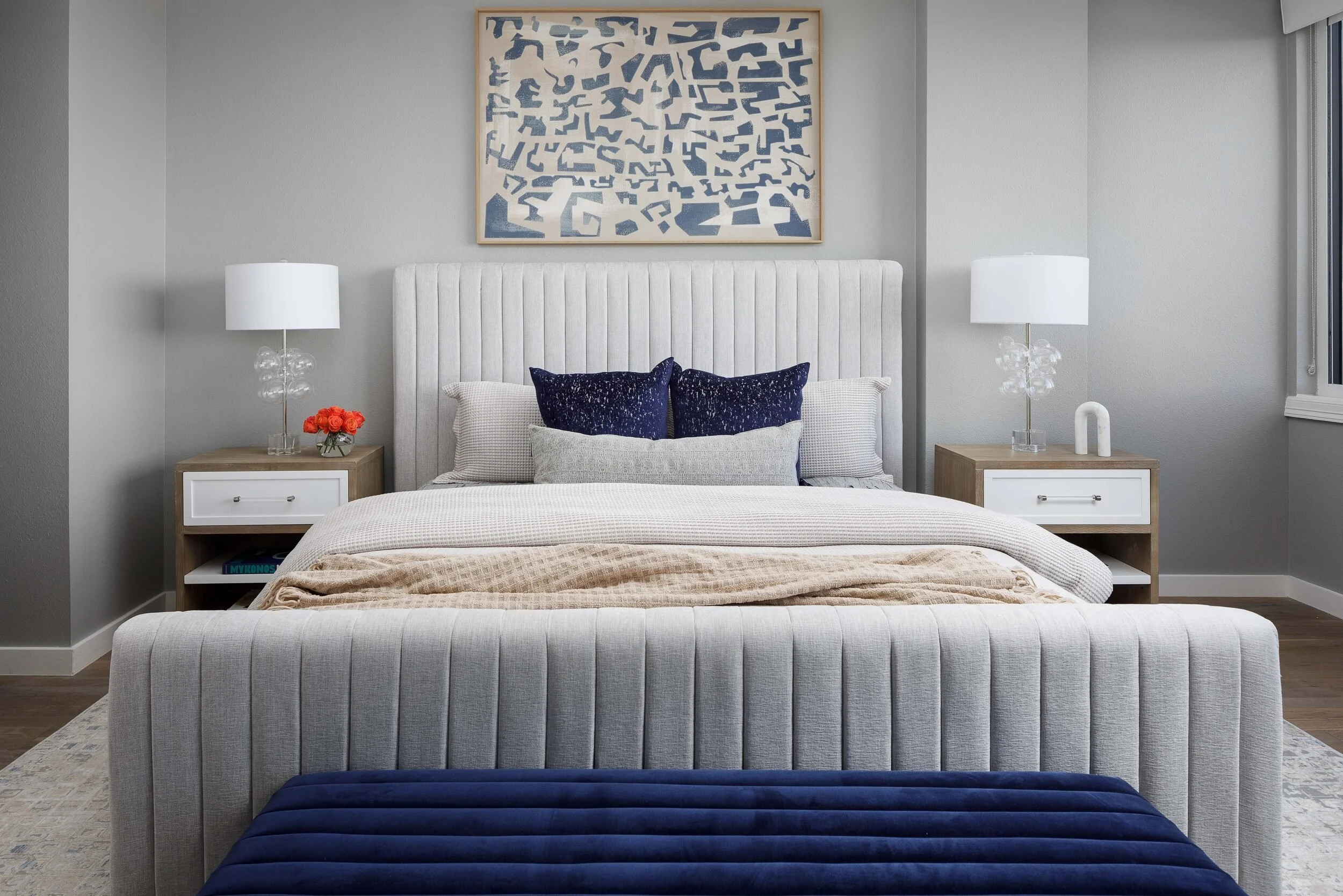 Straight-on view of a channel-tufted bed with navy pillows beneath abstract art