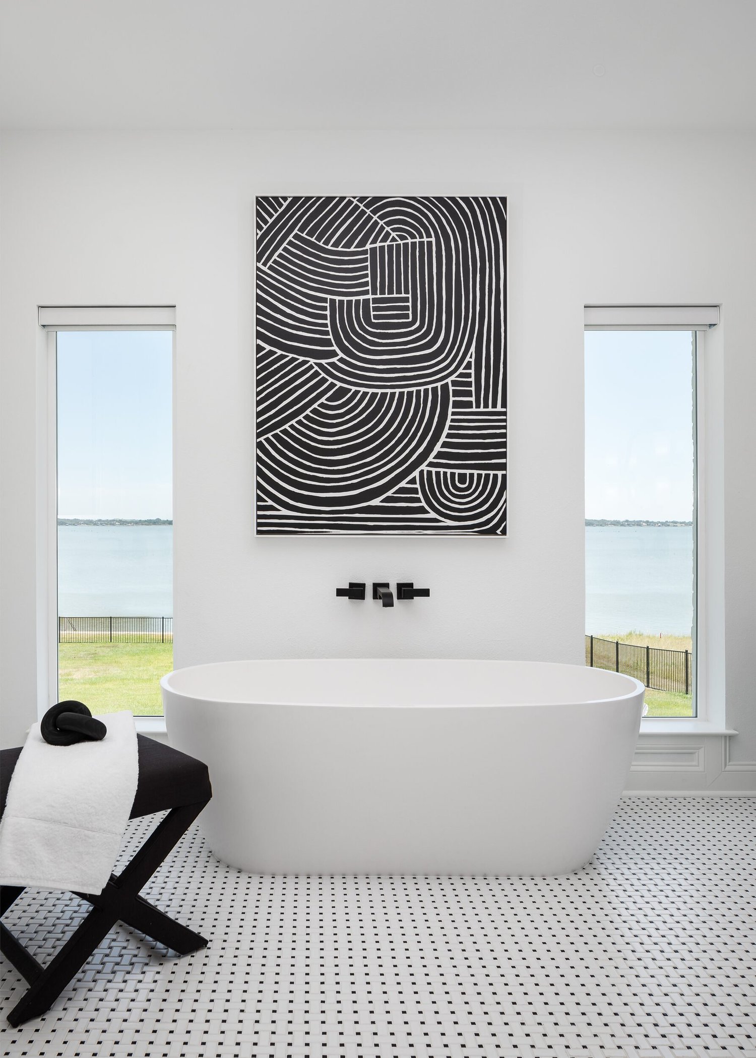 Freestanding tub between two windows overlooking Cedar Creek Lake, below a black and white line painting