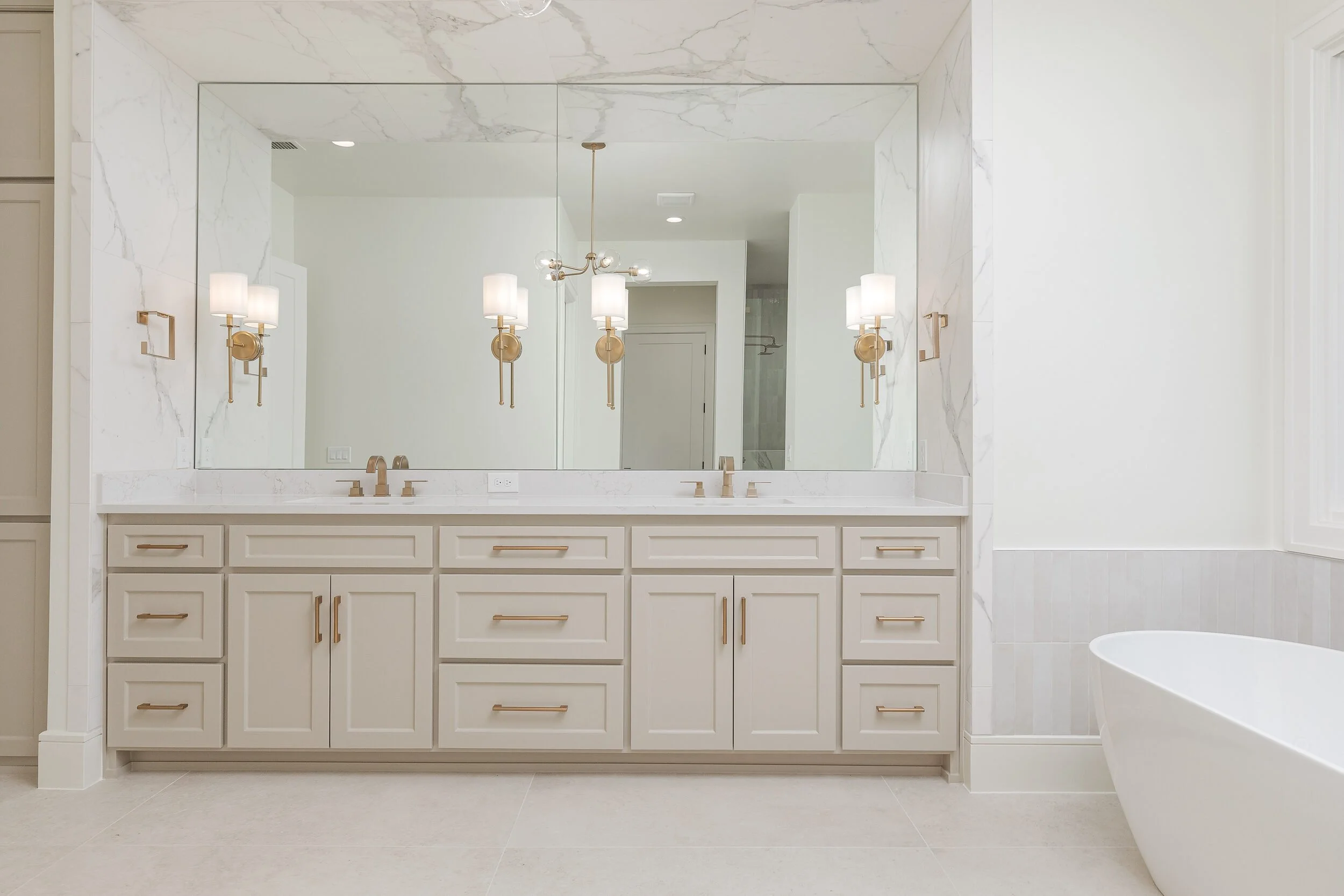 Double vanity with a full-width mirror, brass sconces and marble wall cladding