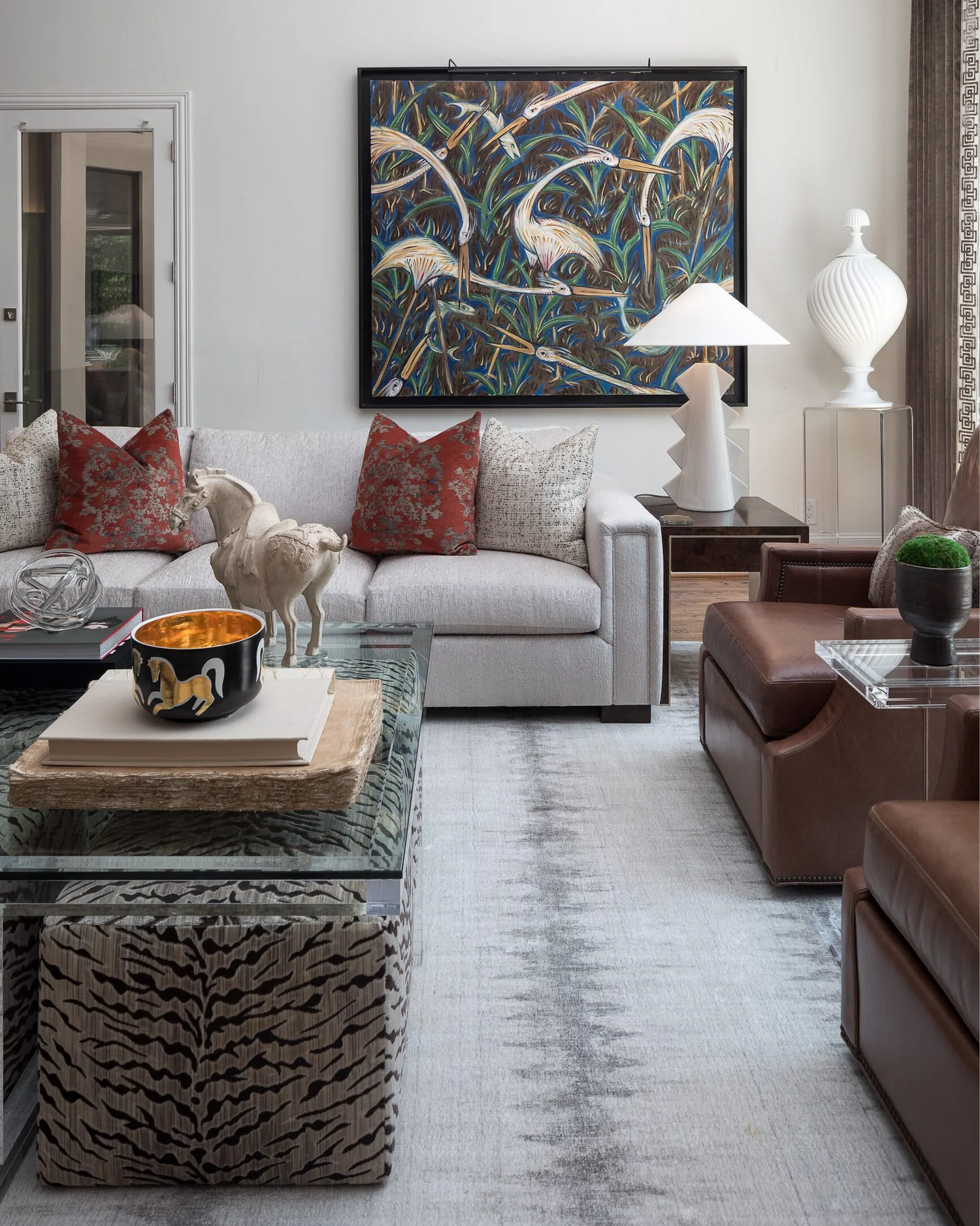 Sofa vignette beneath a heron painting with white ceramic lamps and red accent pillows