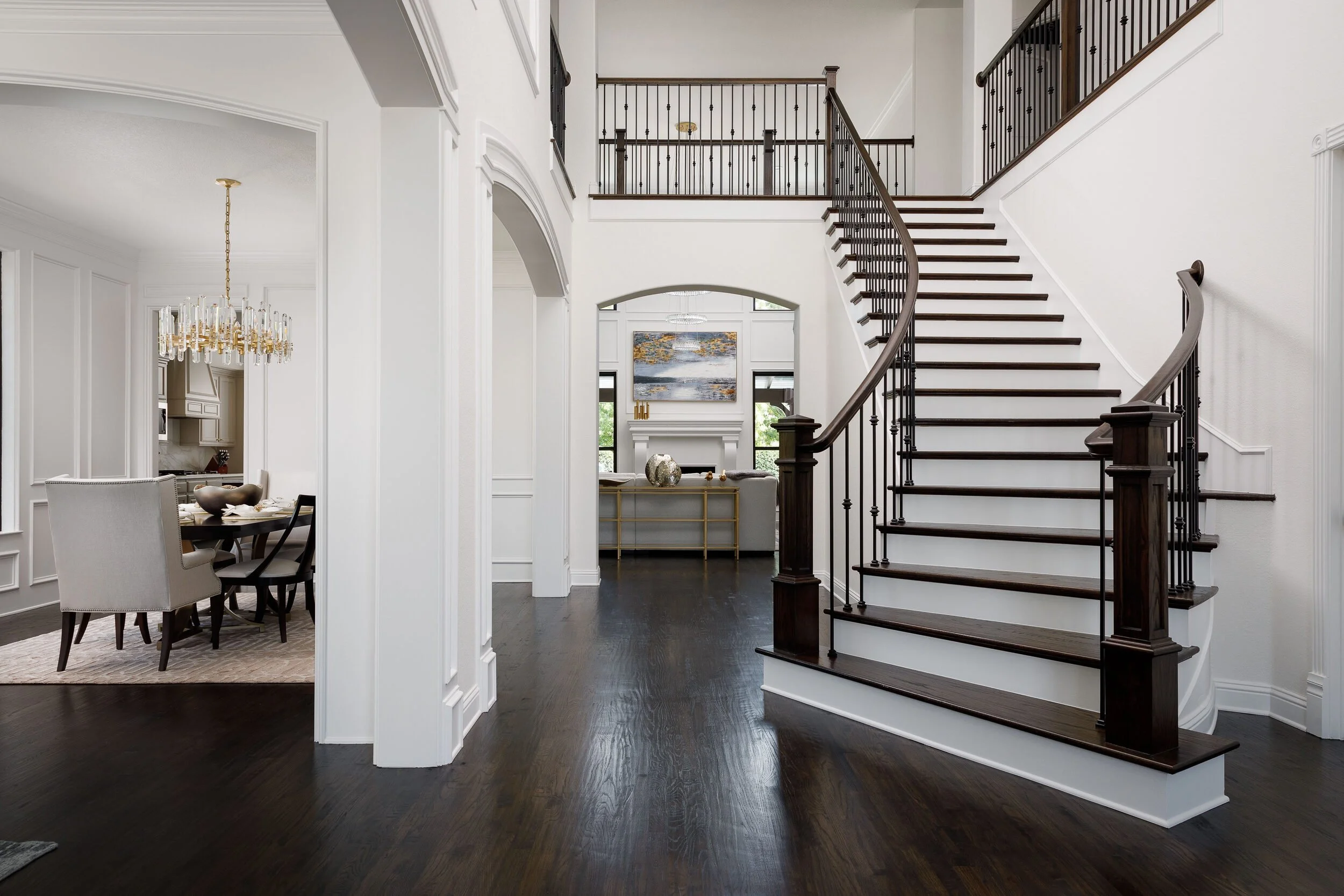 Entry hall with a curved staircase, dark wood floors and a view into the dining room