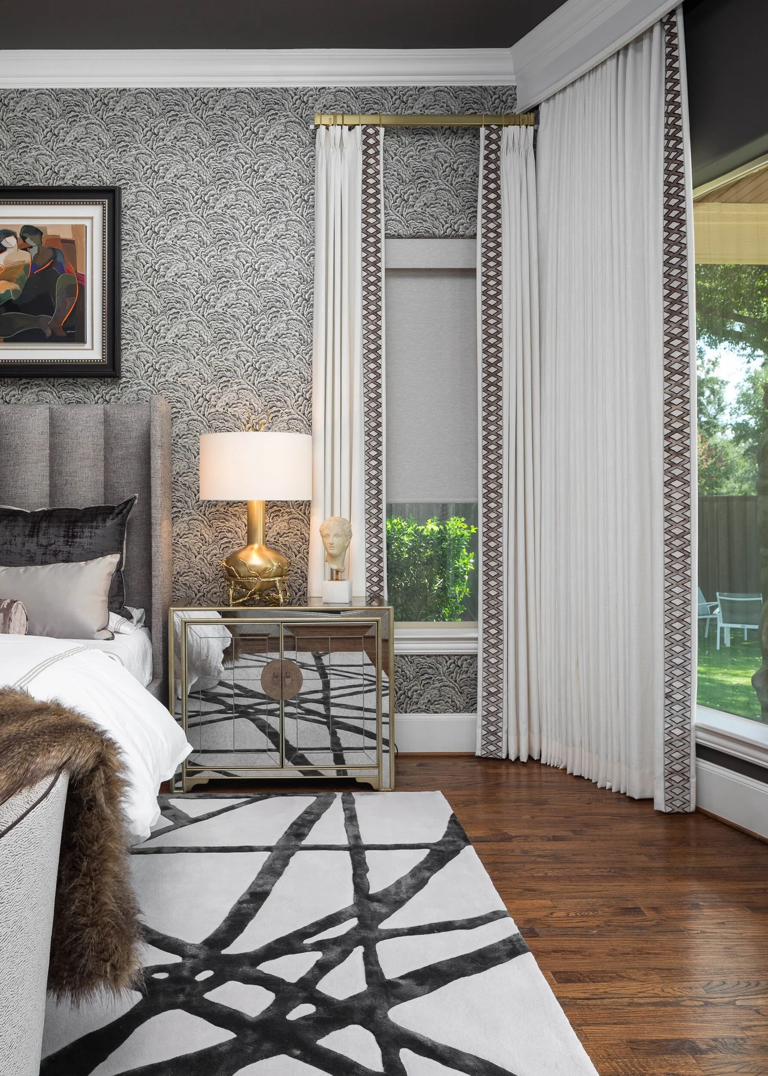 Bedside vignette with a brass lamp, mirrored nightstand and sheer drapery at the window