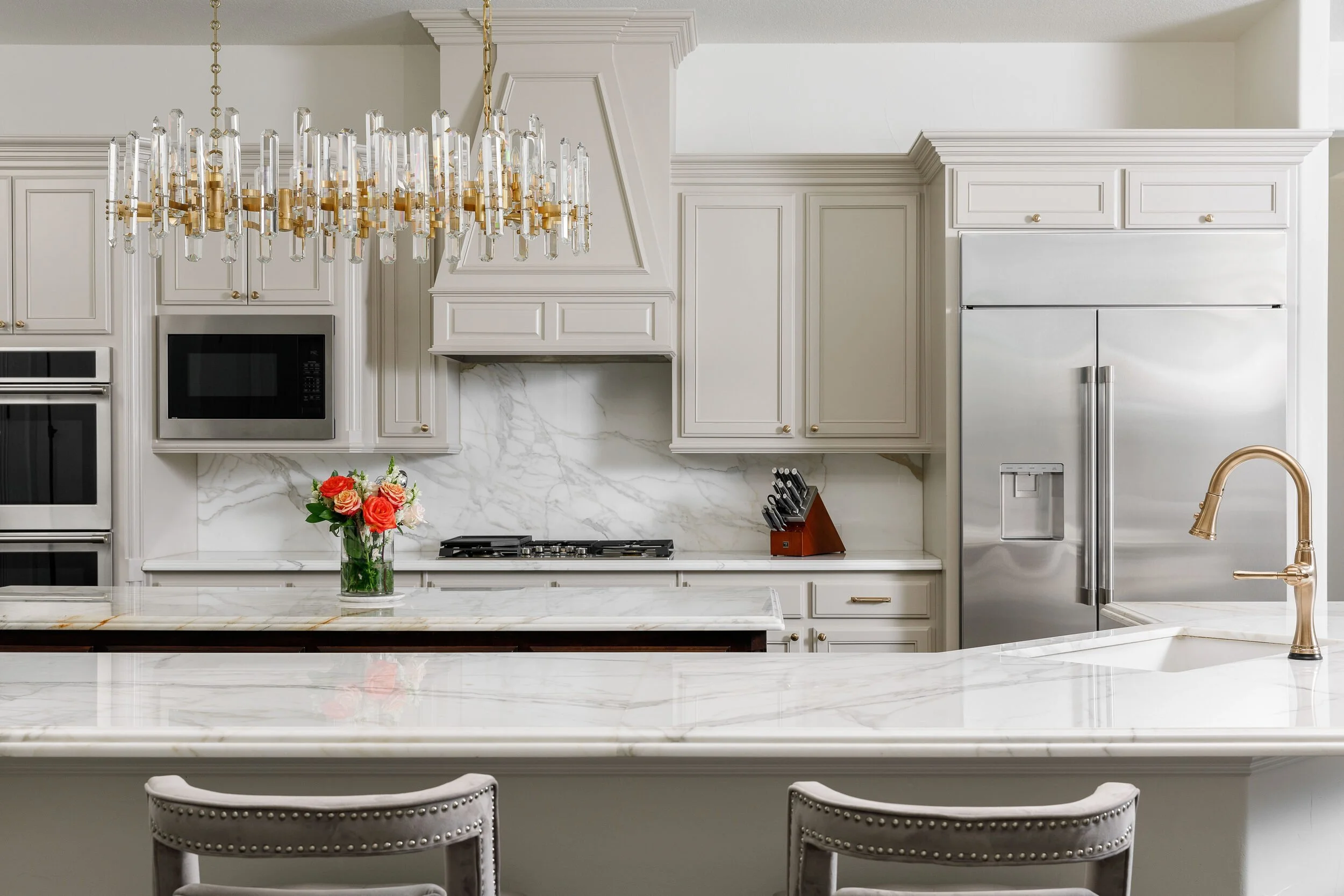 Kitchen with a marble island, brass faucet, stacked ovens and a built-in refrigerator