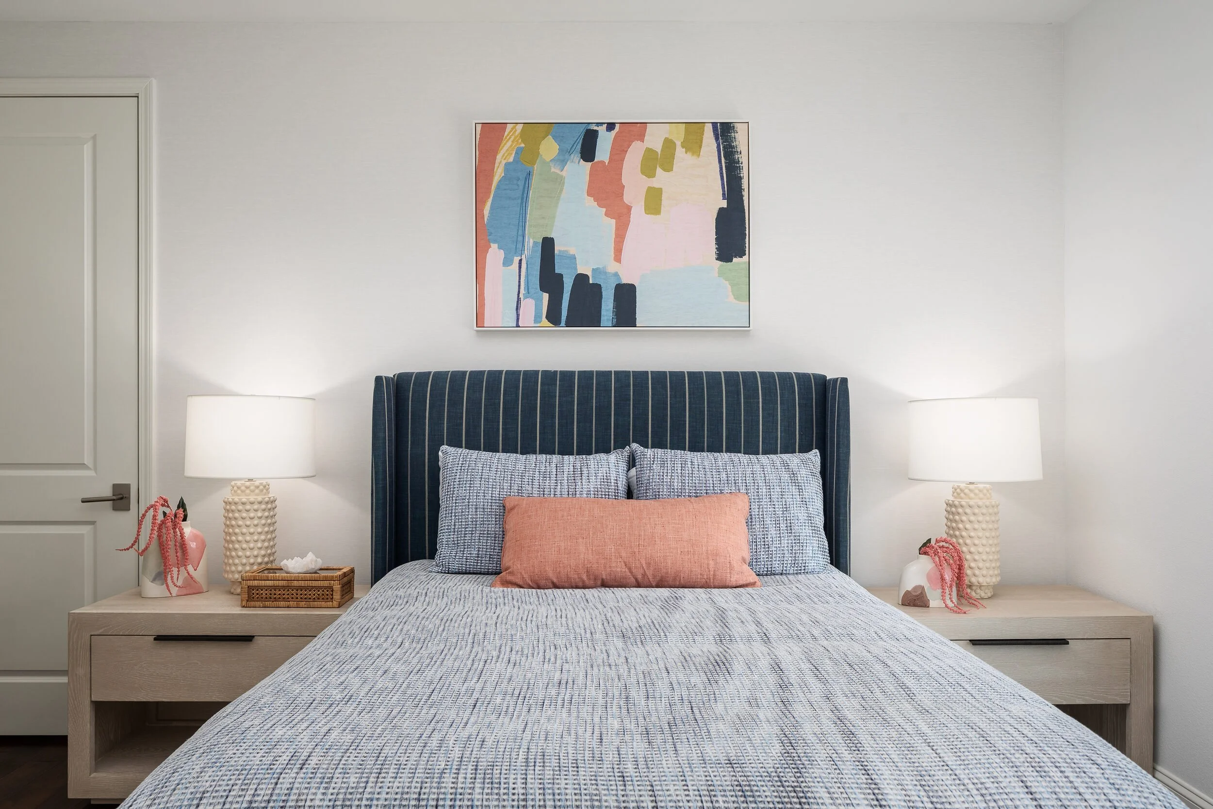 Bedroom with a navy striped headboard, coral pillows and colorful abstract art