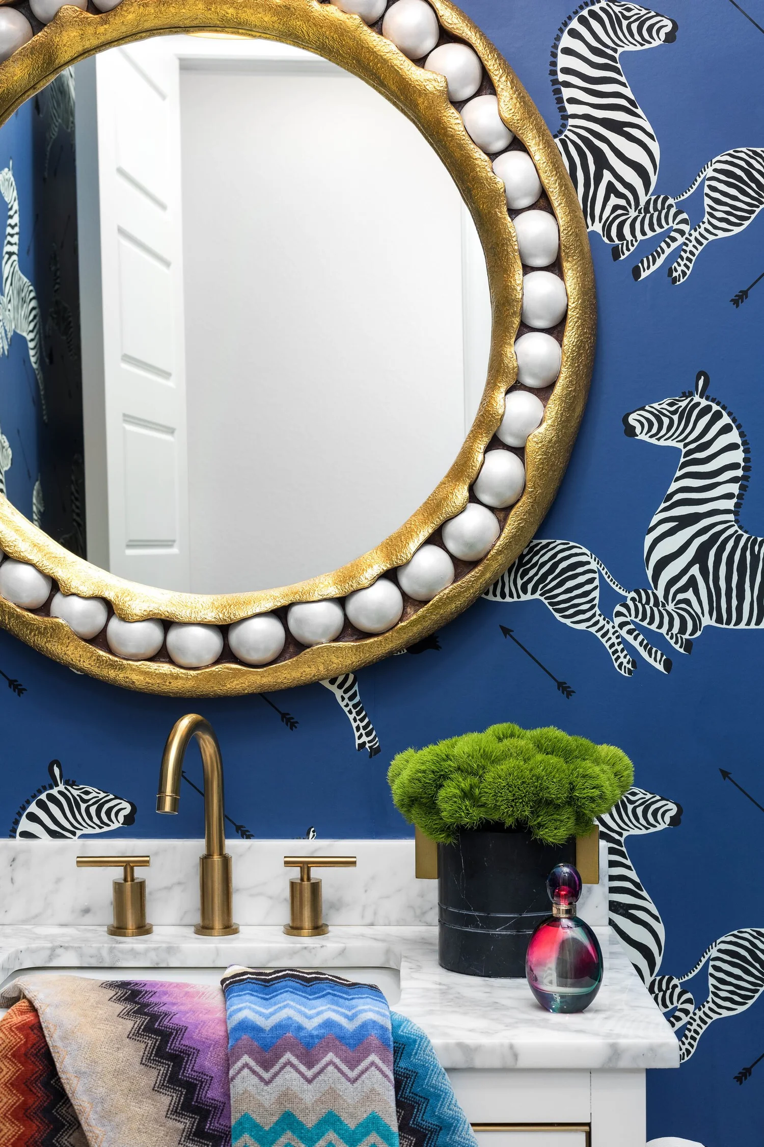 Detail of the gold beaded mirror, brass faucet and zebra wallpaper