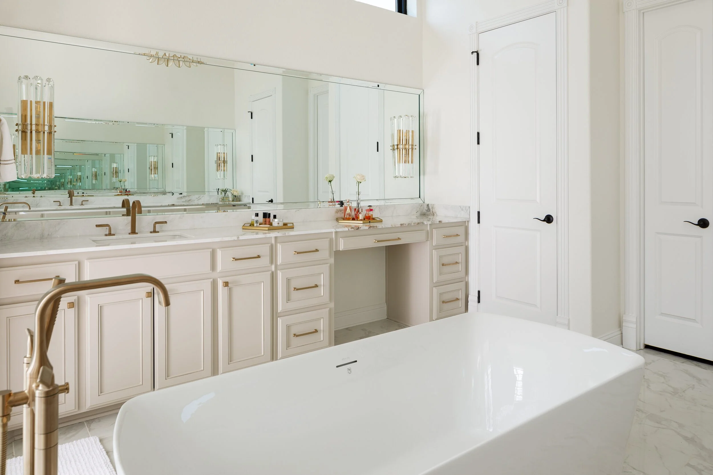 Primary bath vanity wall with brass sconces, a long mirror and a freestanding tub