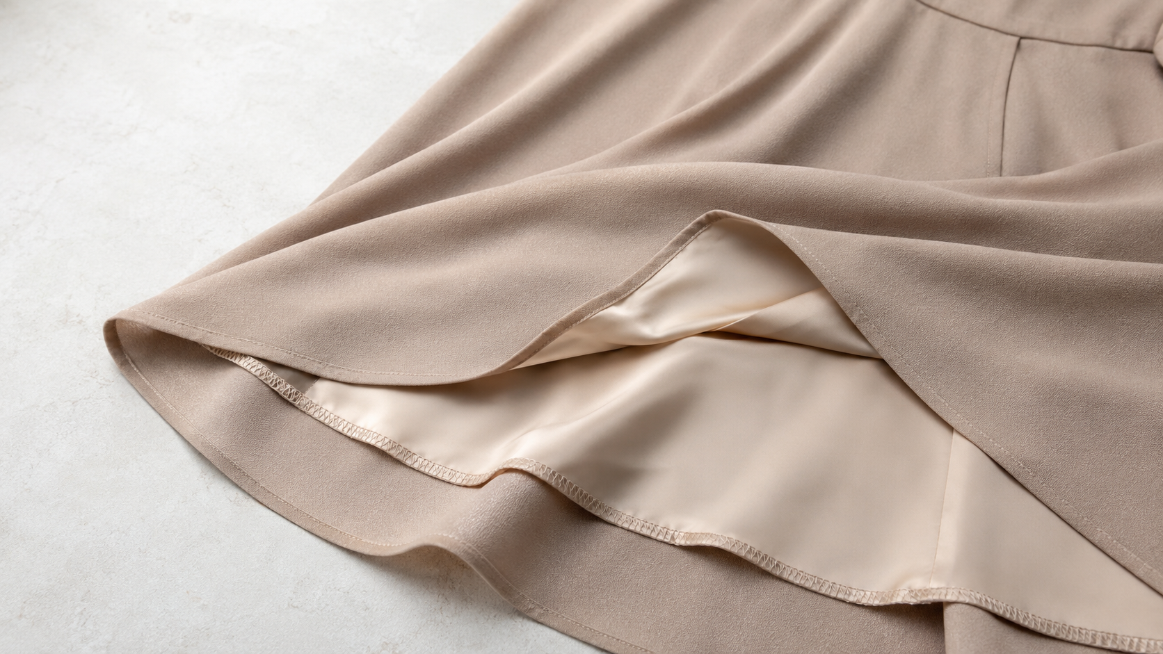 Close-up of fabric drape and lining construction detail on a dress, showing how the outer fabric and lining interact at the hem and seam