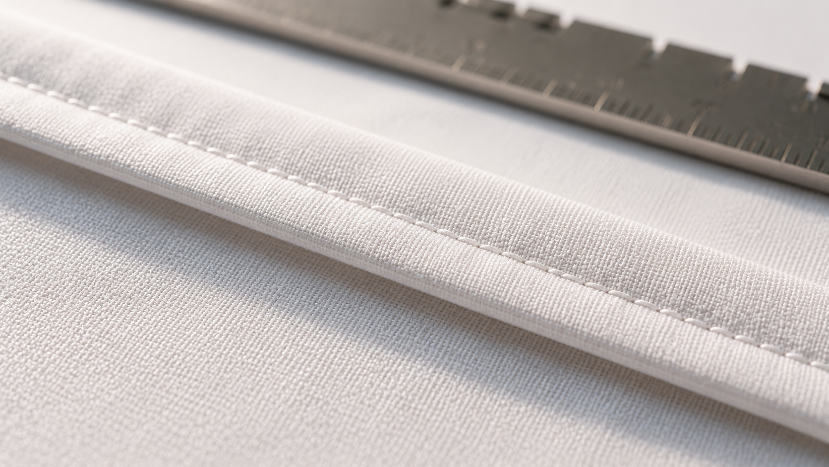 Close inspection of a double-folded hem on a white institutional sheet showing even stitch density