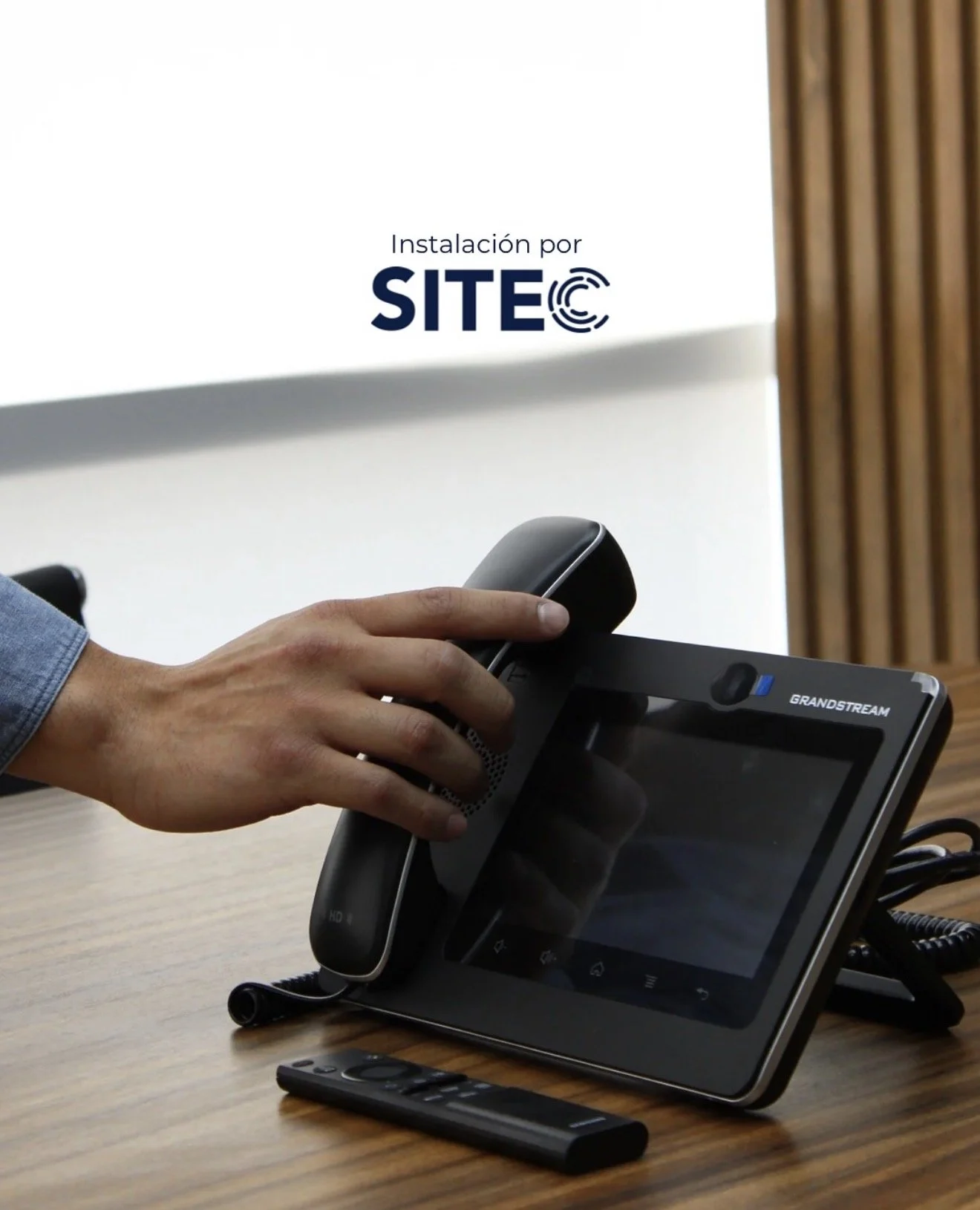 Publicación de SITEC con una persona tomando el auricular de un teléfono Grandstream sobre un escritorio.
