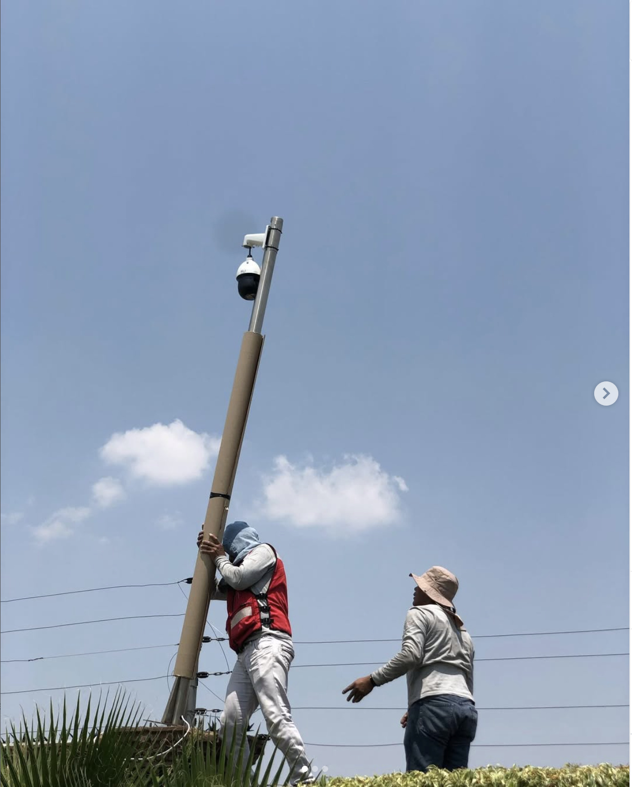 Dos técnicos trabajando en un poste con una cámara de videovigilancia exterior.