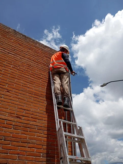 Técnico sobre una escalera trabajando junto a un muro exterior de Conalum.