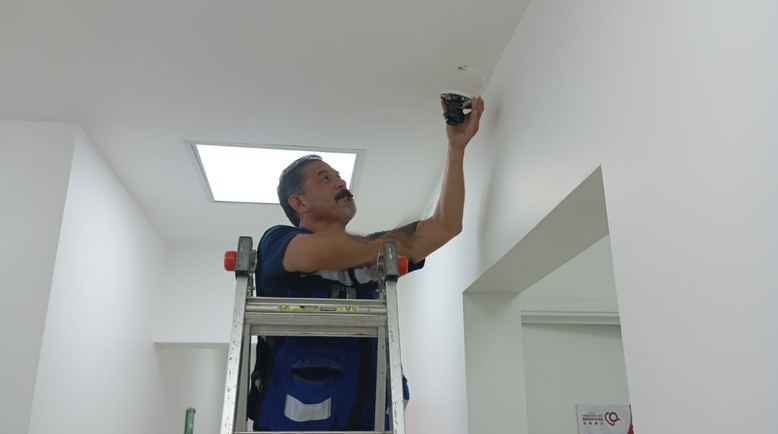 Técnico sobre una escalera colocando una cámara en el interior de una Unidad del Bienestar en Quintana Roo.
