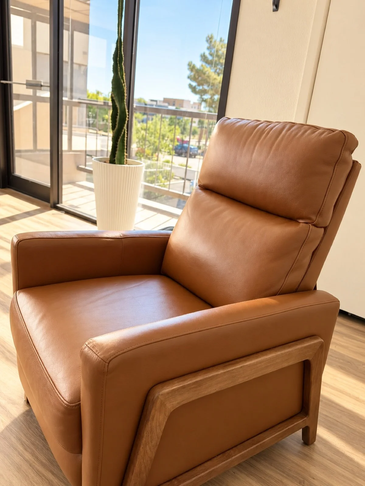 Brown leather lounge chair beside a sunlit window at ATRIUM