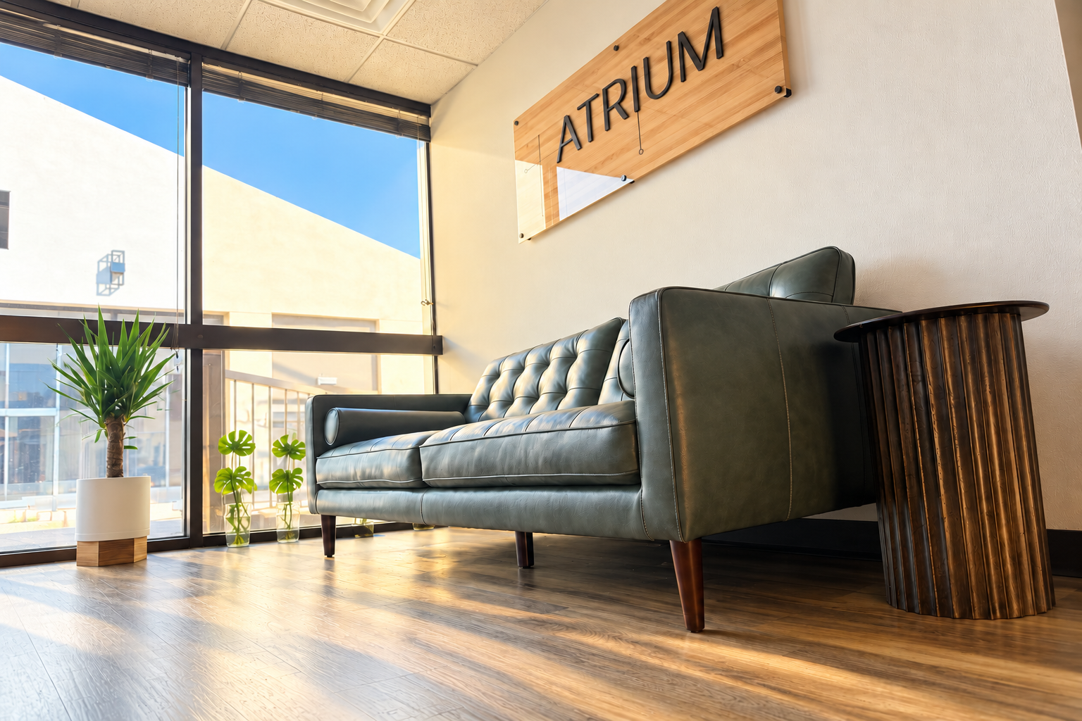 The ATRIUM waiting lounge in Scottsdale: a leather sofa under the wooden ATRIUM sign, with potted plants and sunlight from tall windows