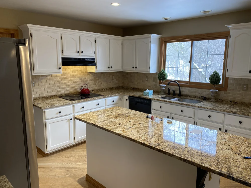 Finished kitchen with white-painted cabinets, a granite island, and warm wood floors by Quality Over Quantity