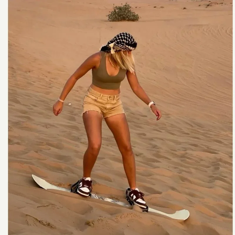 Woman sandboarding the Dubai desert dunes at golden hour