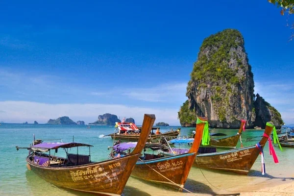 Longtail boats on turquoise water with limestone cliffs in Thailand