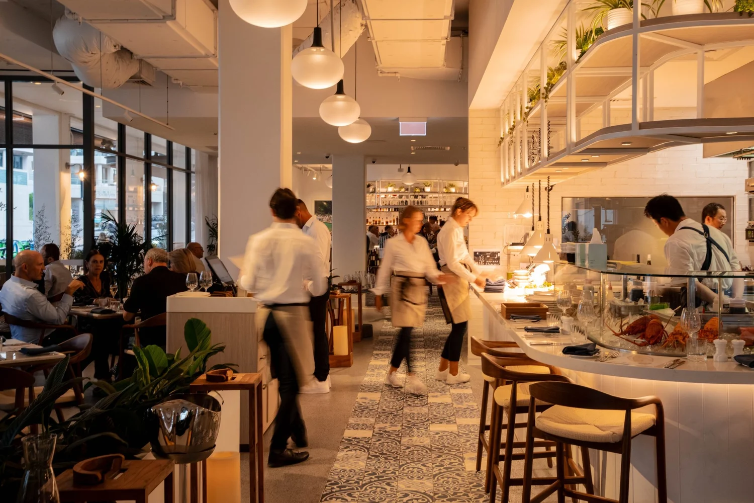 The dining room at Rick Stein at Coogee Beach during service, staff passing the open kitchen.