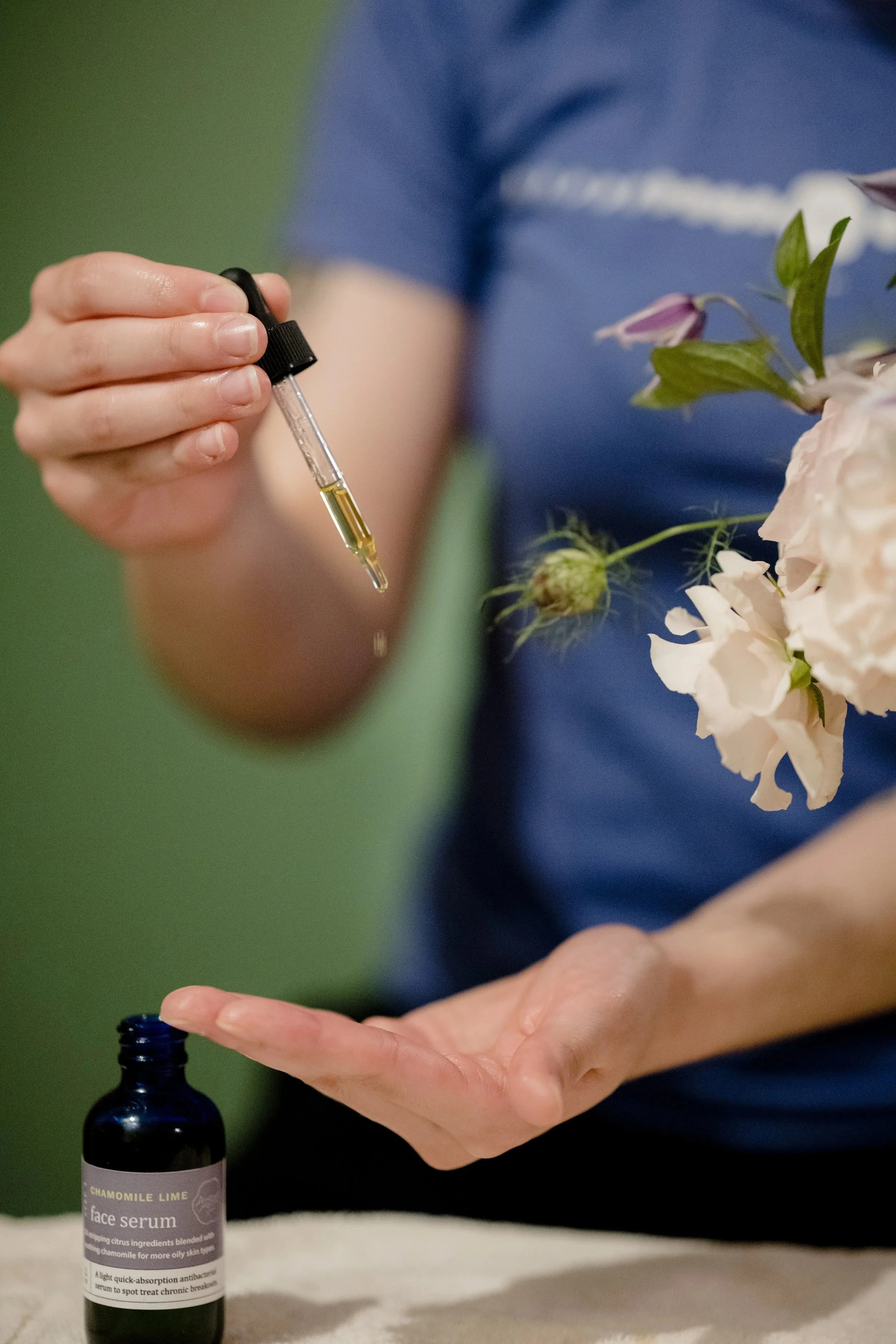 A dropper of oil held beside fresh flowers at August Moon Spa