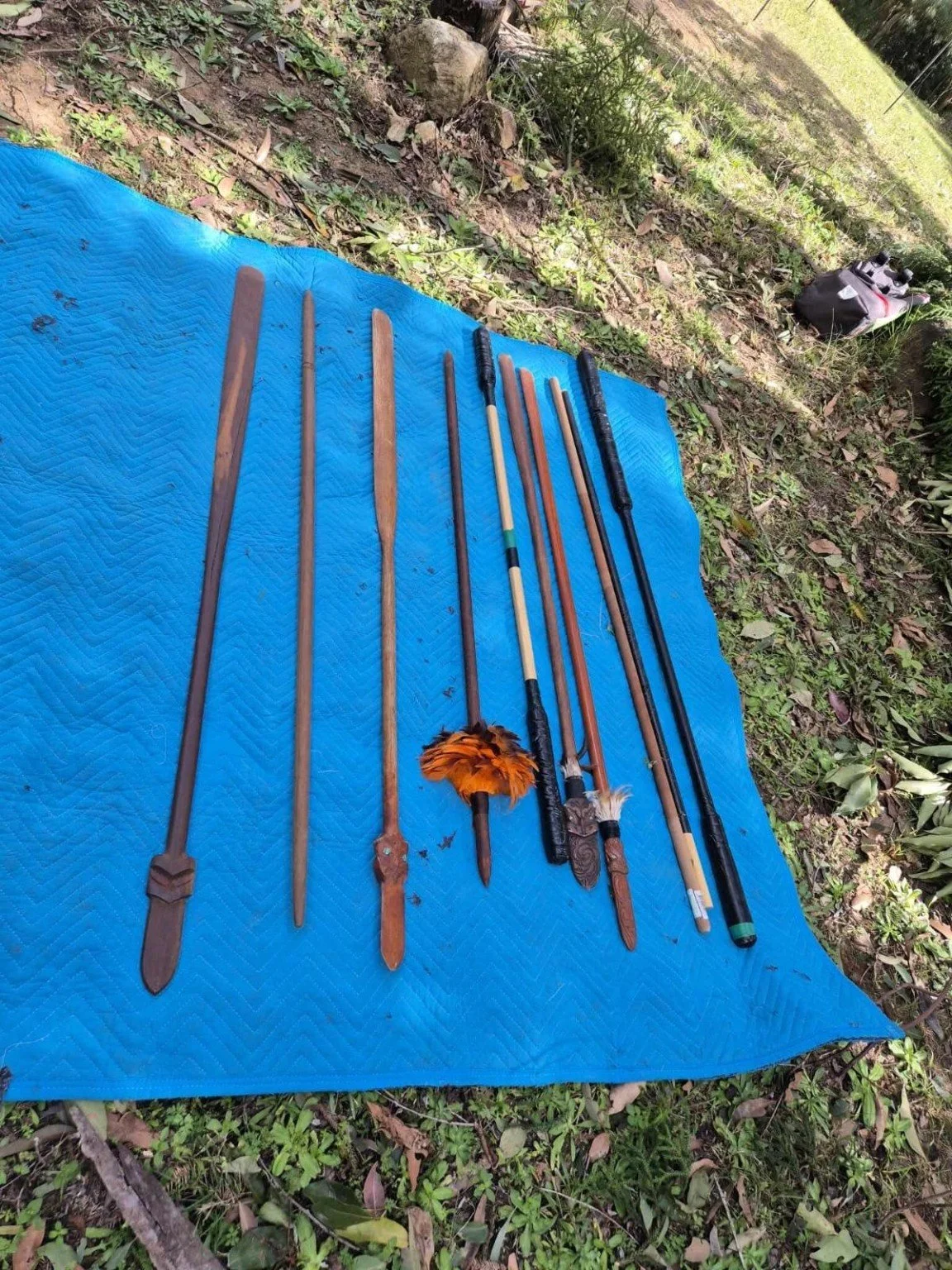 Carved wooden staffs and long-handled implements arranged on a blue mat outdoors.