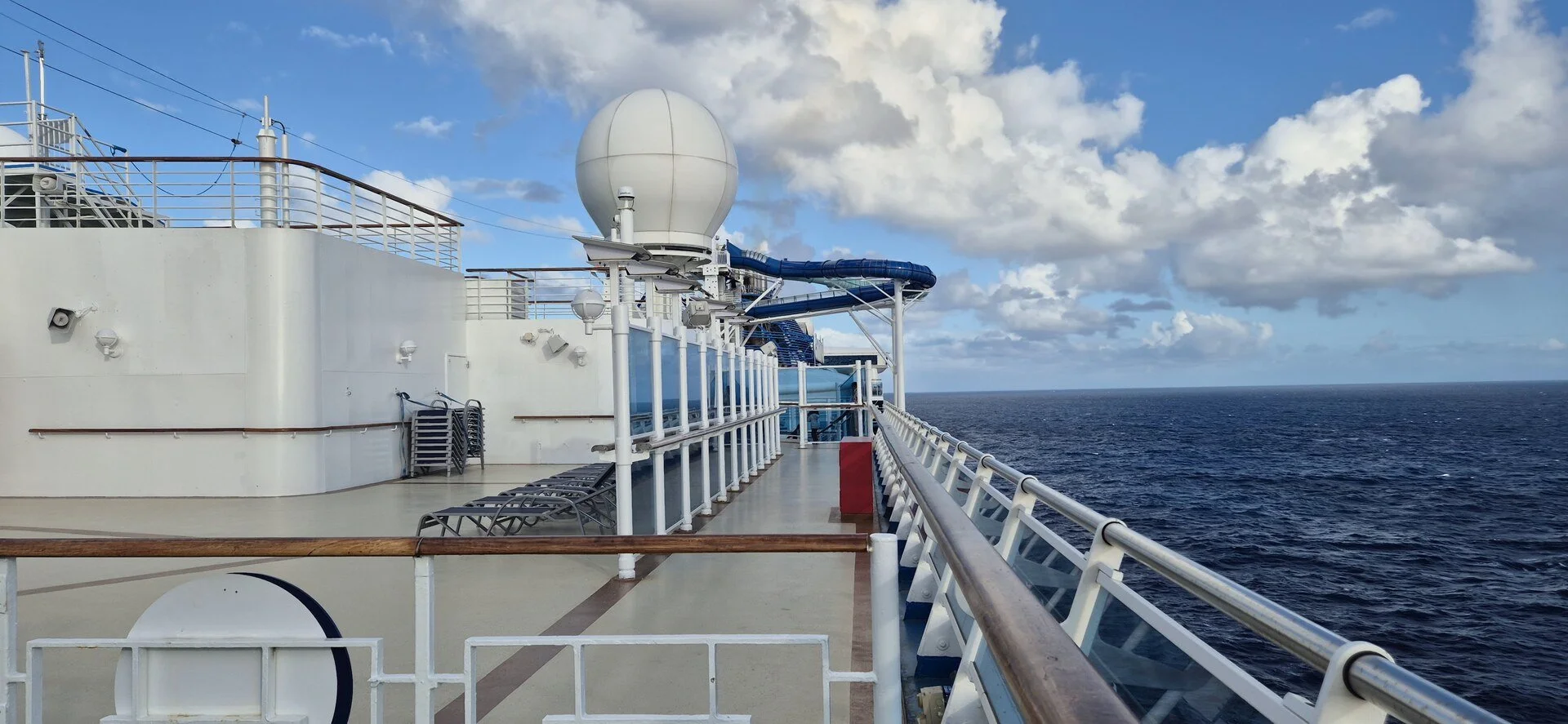 Cruise ship deck overlooking the ocean under blue skies.