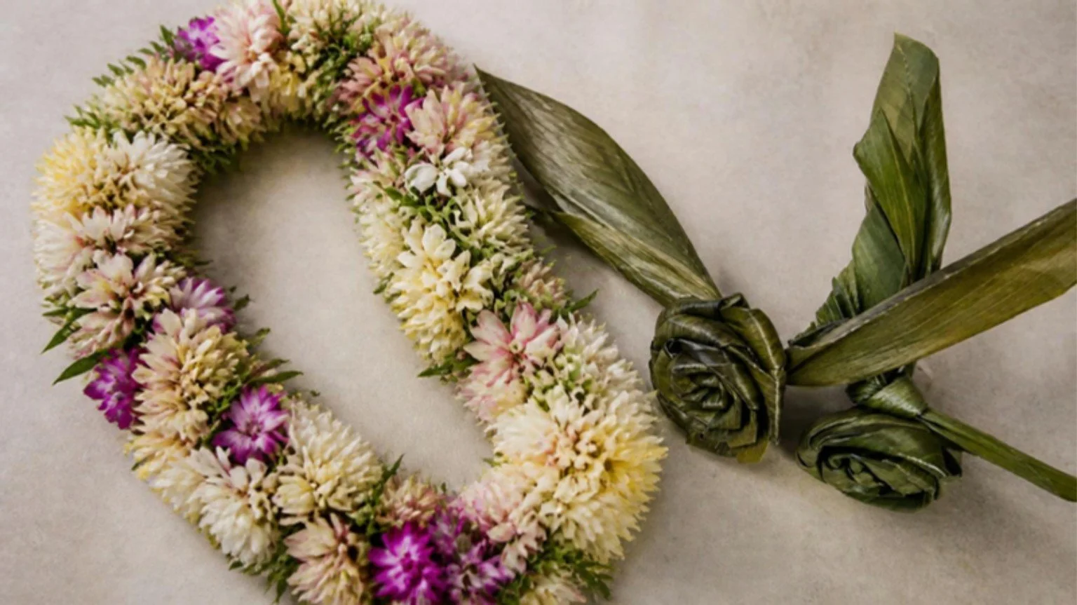 A flower lei beside decorative woven green leaves.