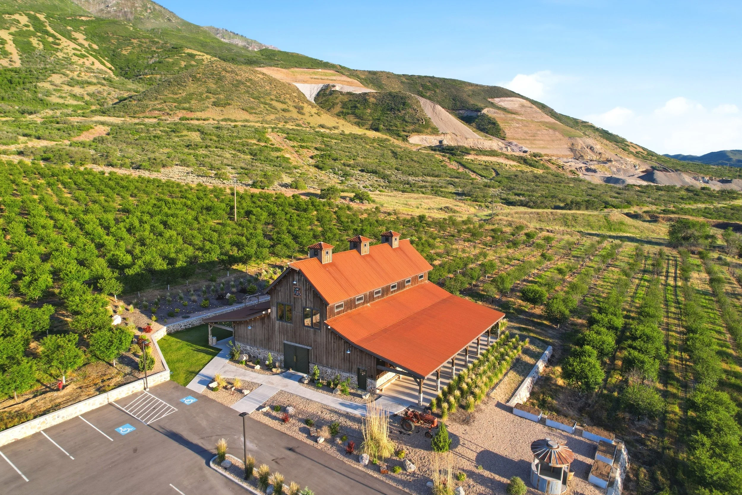 Aerial view of a barn style building surrounded by orchard trees and Utah mountain foothills