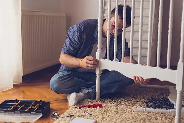 Dad assembling baby crib — preparing before baby arrives