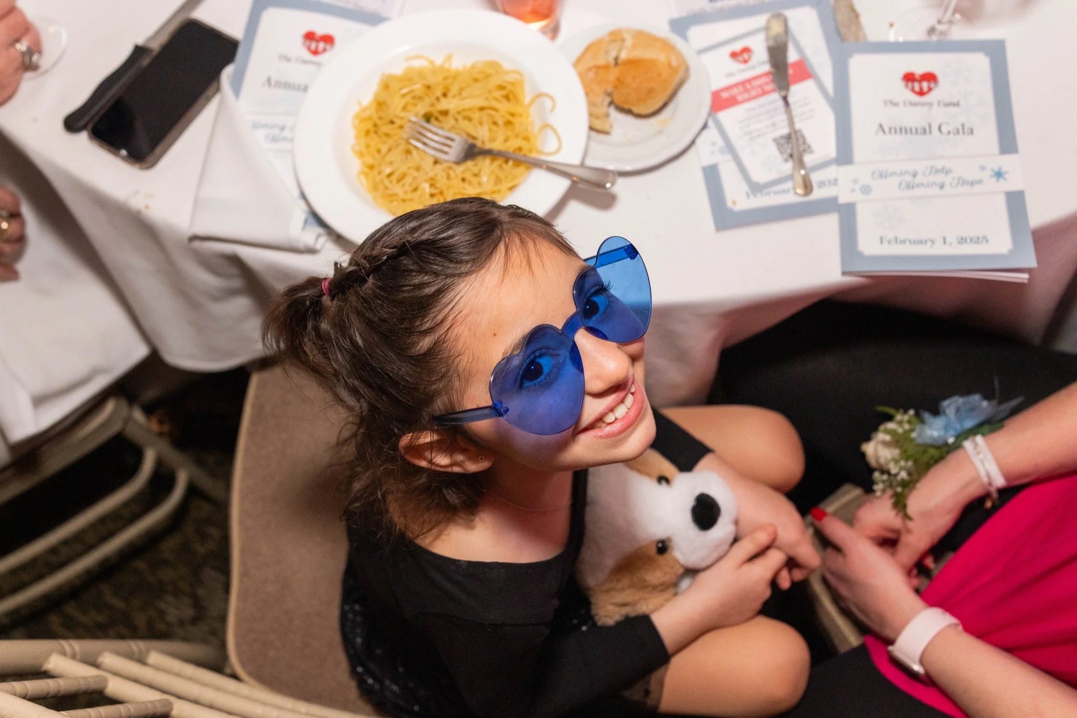 Young gala guest smiling in oversized blue heart-shaped glasses