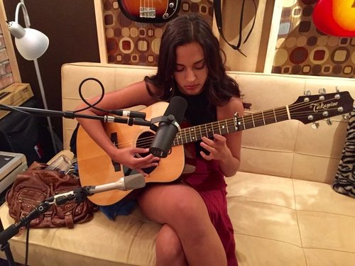 Songwriter recording an acoustic guitar part on a couch