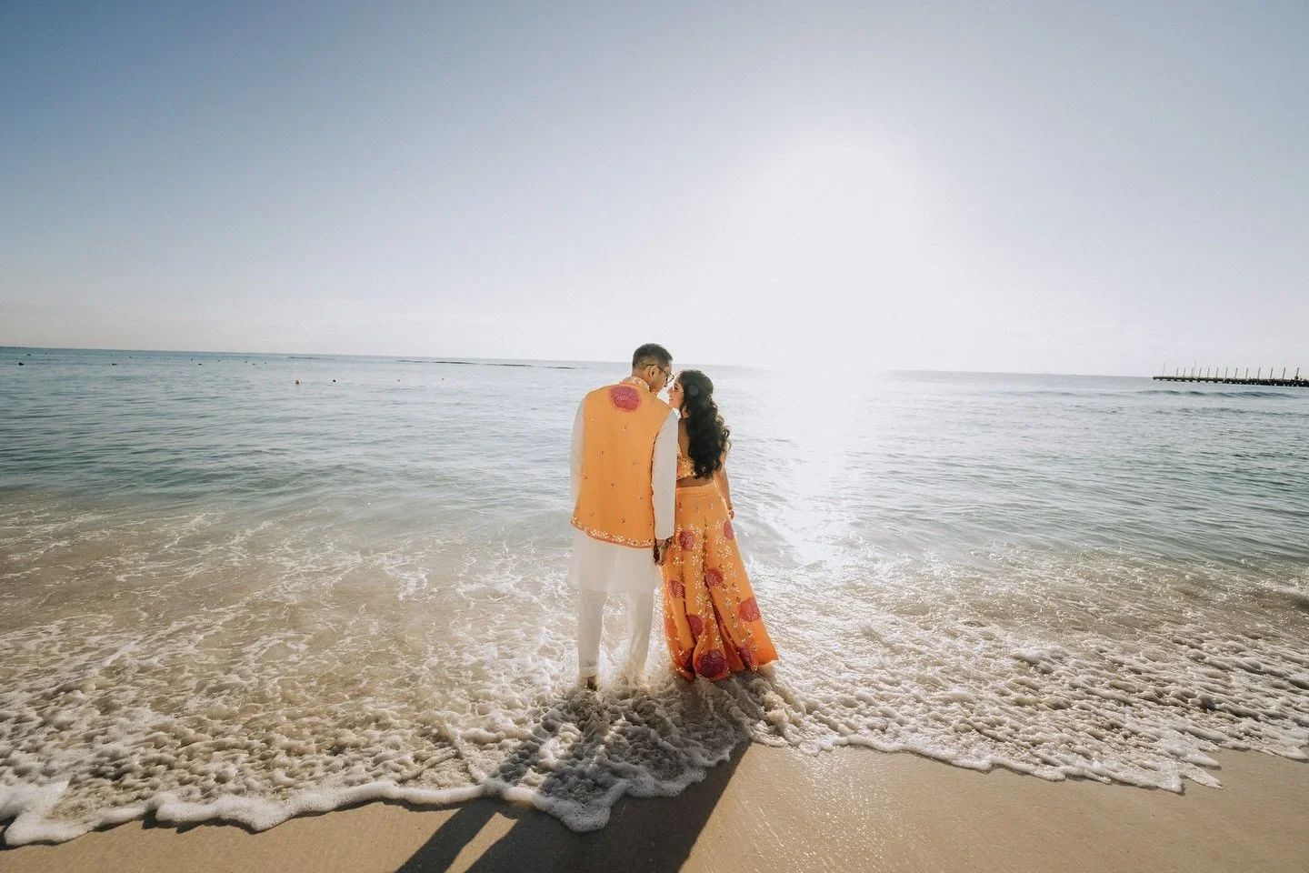 Couple in traditional attire standing on a beach at the water's edge