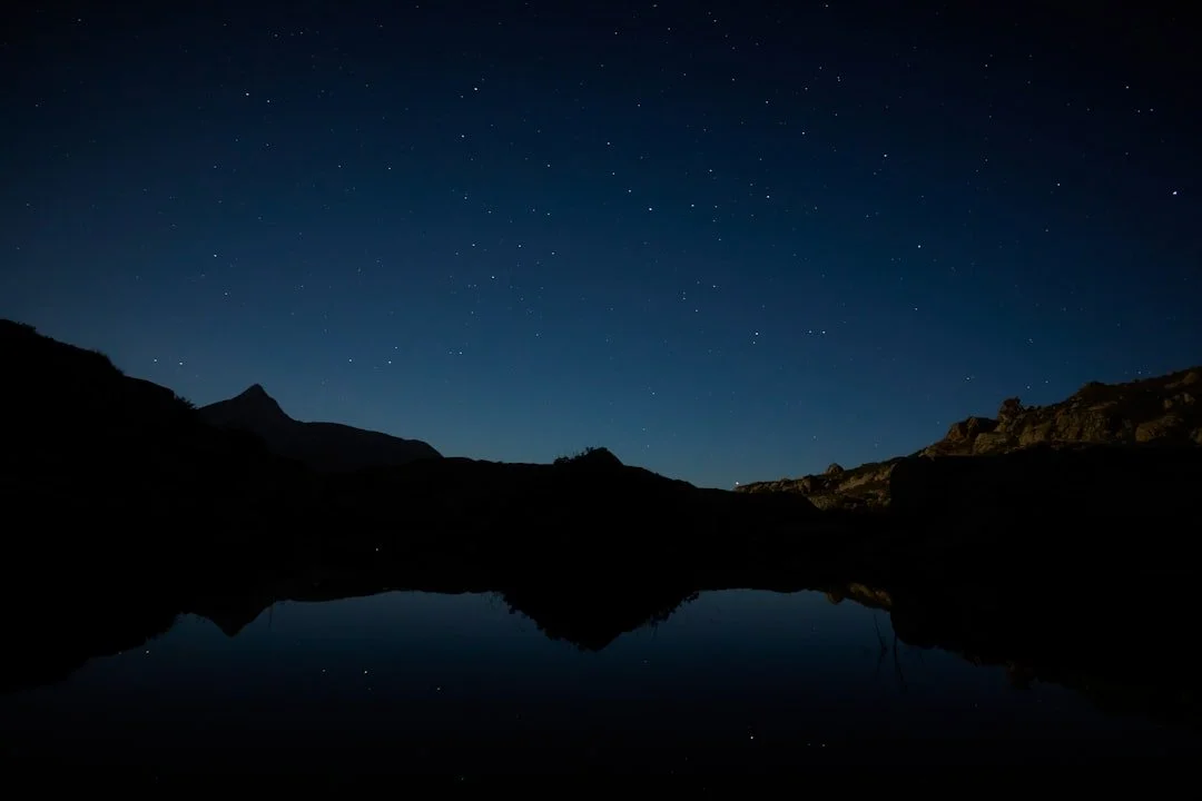 A starry night sky above a dark mountain lake with reflections