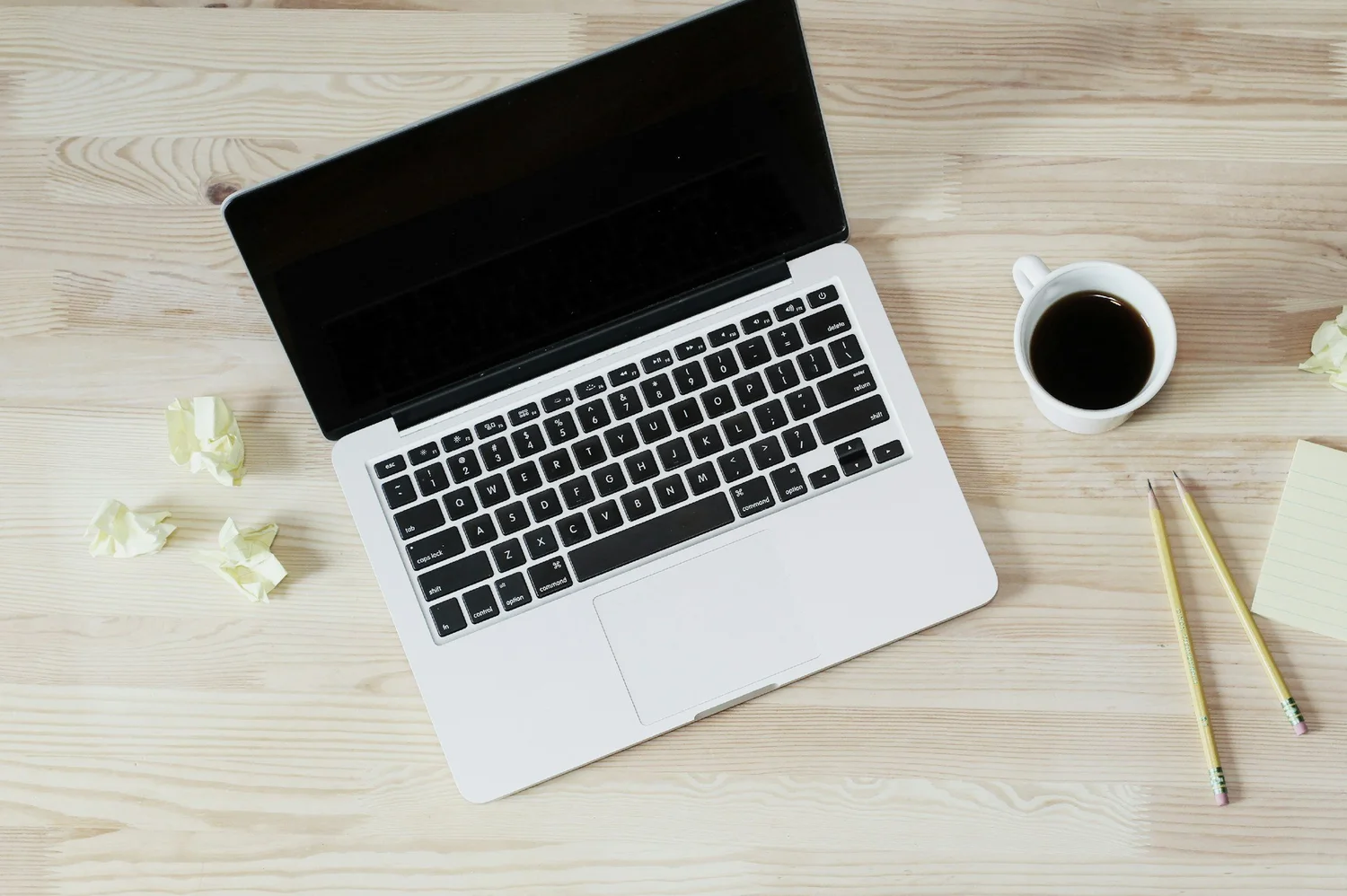 A laptop and coffee on a light wooden desk