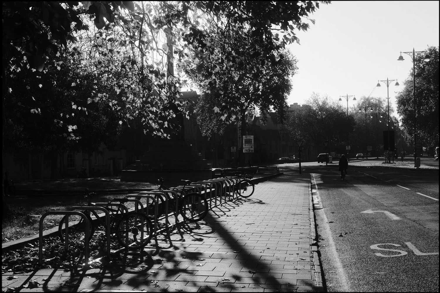 Black and white photo of an empty Oxford street under dappled morning light, with a distant figure walking.