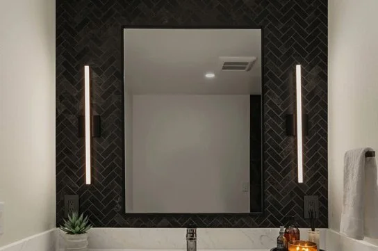 Backlit mirror with vertical sconces over vanity and black herringbone tile—modern lighting plan in Maple Valley, WA