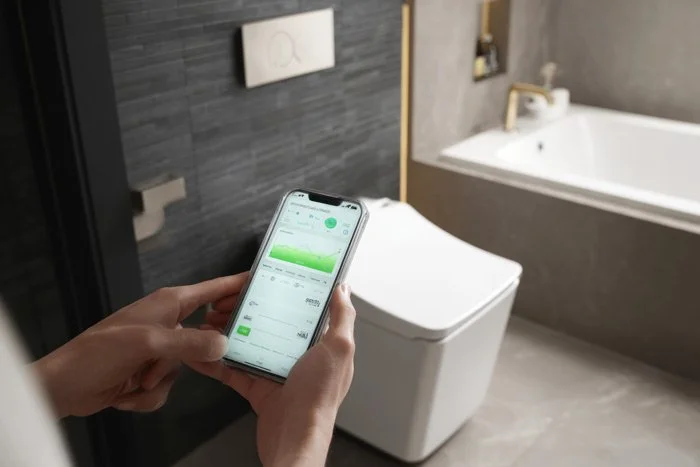 Smartphone controlling bathroom features near modern toilet—heated floors and tech amenities in a Bellevue, WA renovation
