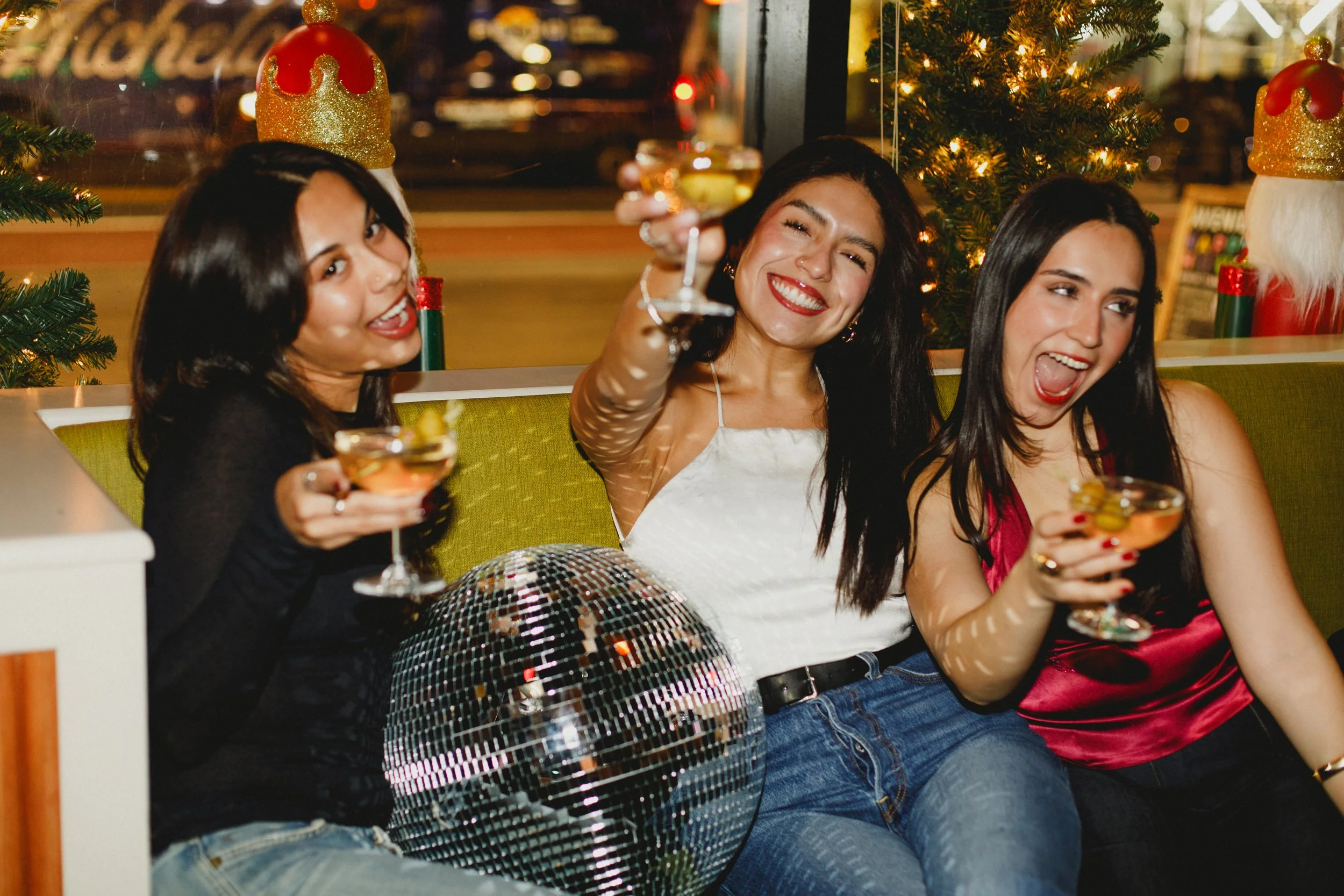 three women celebrating indoors with all holding martinis towards the camera
