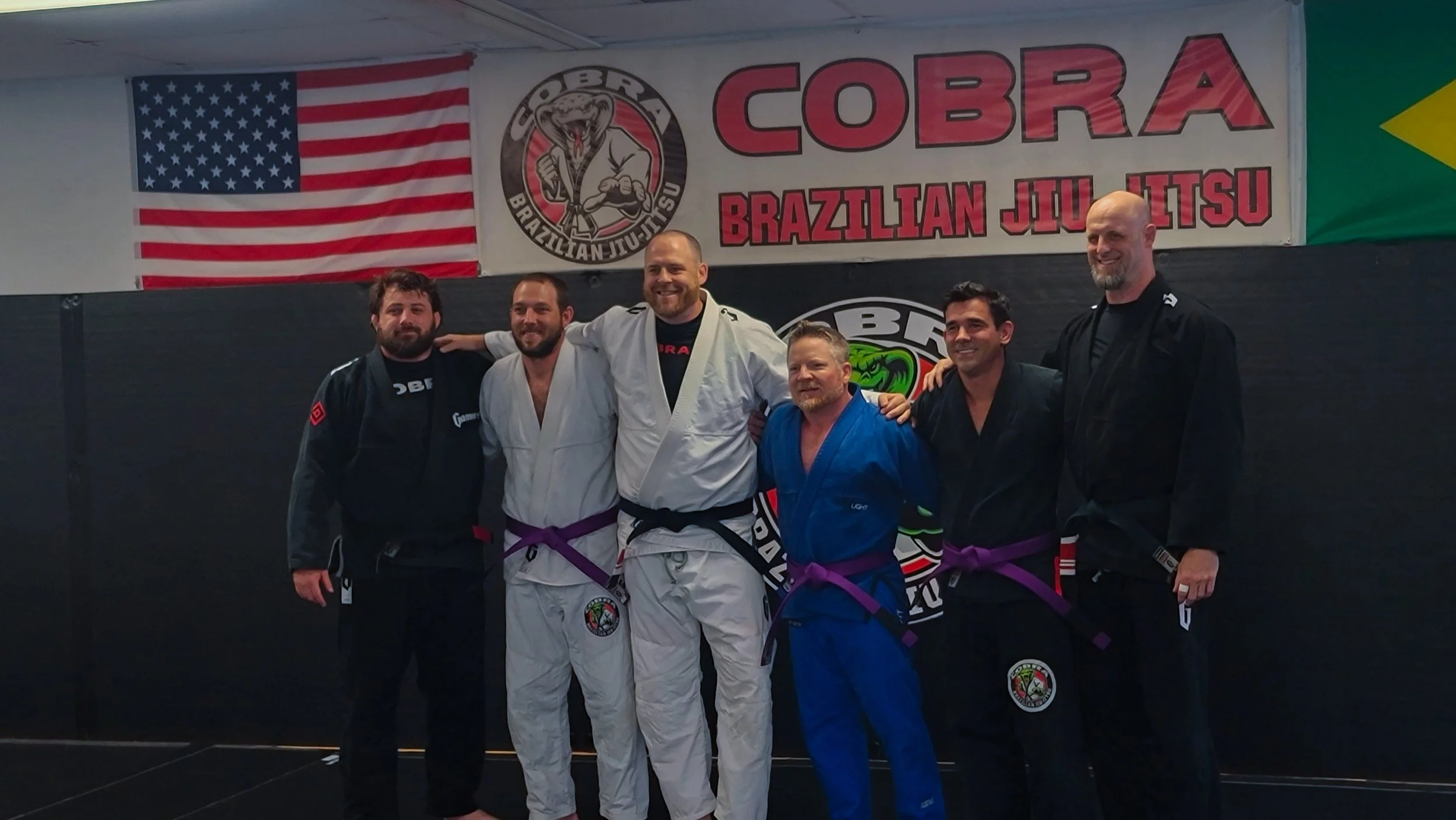 Cobra BJJ Mansfield team lined up under the gym banner after a belt promotion