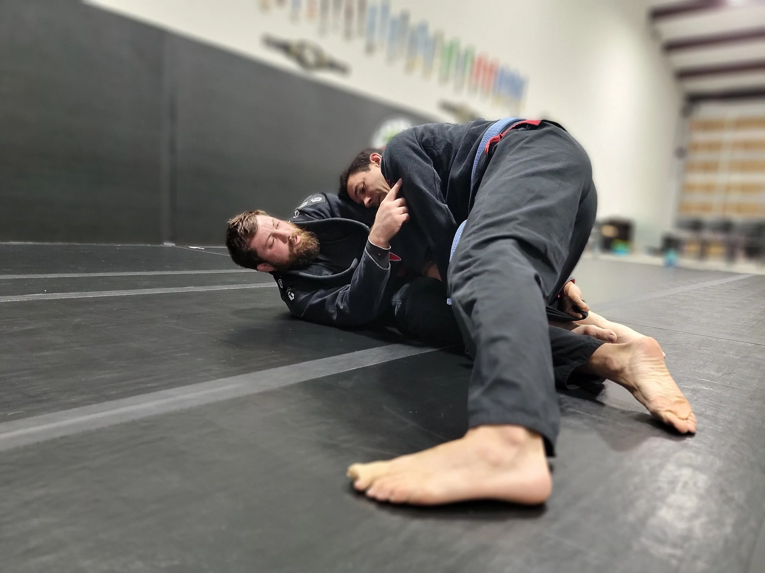 Two students rolling on the mat at Cobra BJJ Mansfield, medals on the wall behind them