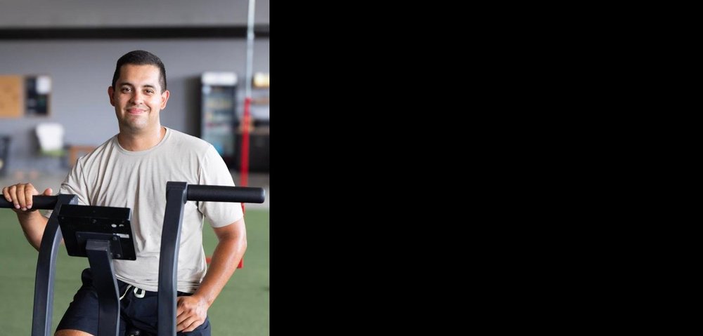 Ty, Einhorn Training Co. July Athlete of the Month, smiling on an air bike